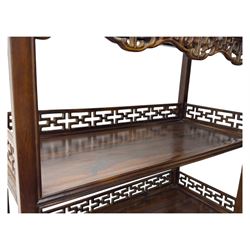 Early 20th century Chinese hardwood display étagère bookcase, the rectangular open tiered frame with pierced frieze and geometric openwork gallery to each shelf, fitted with two short drawers carved with stylised lotus motifs, supported on square uprights with pierced apron and integral gallery rails