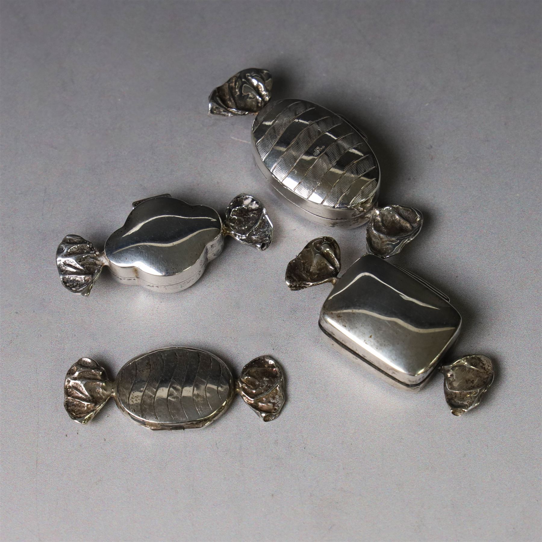 Four novelty silver pill boxes, in the form of wrapped sweets, all hallmarked, largest W6cm