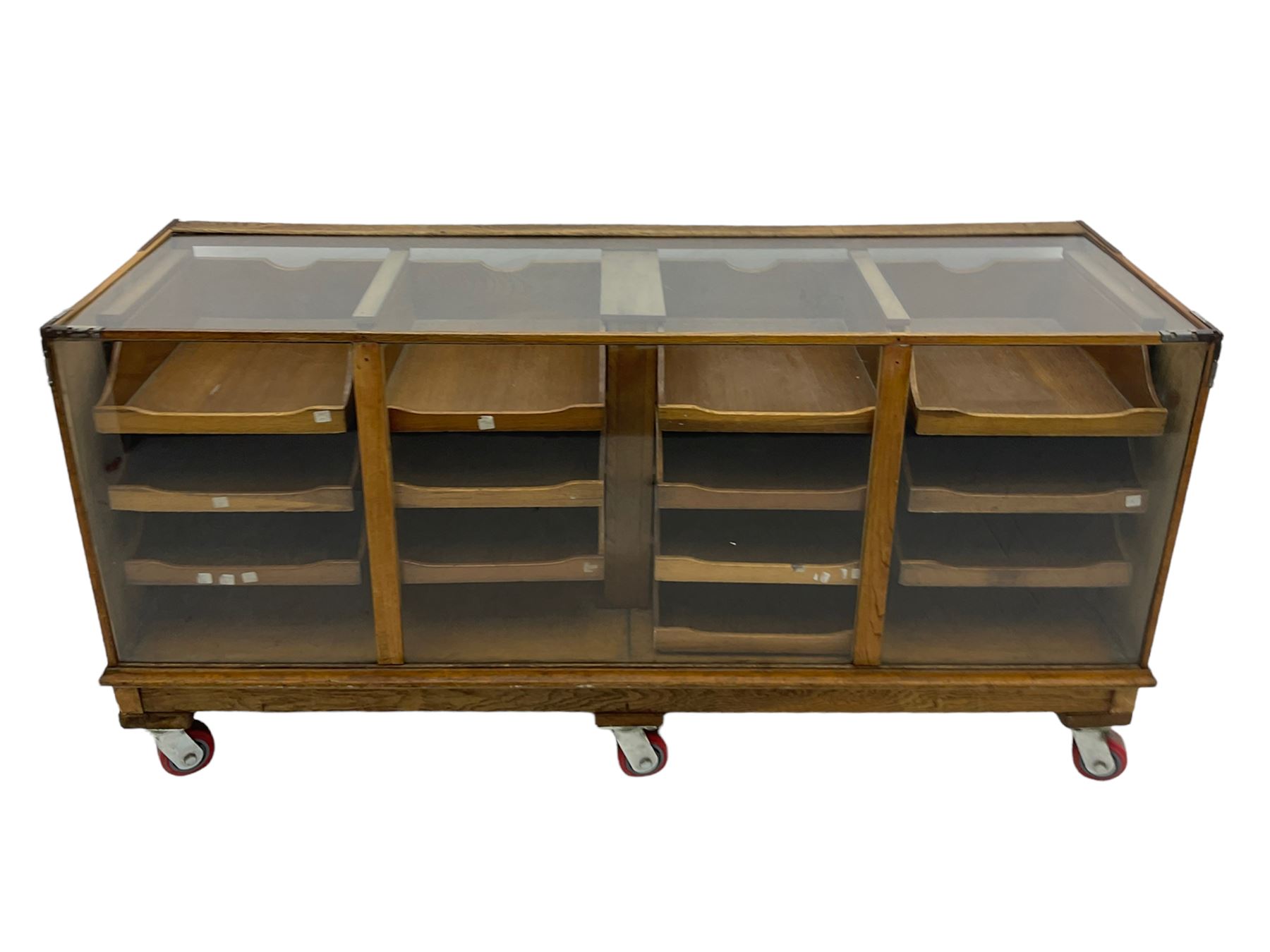 Early 20th century oak framed and glazed haberdashery / shop display cabinet, fitted with sixteen drawers (three missing), on later casters