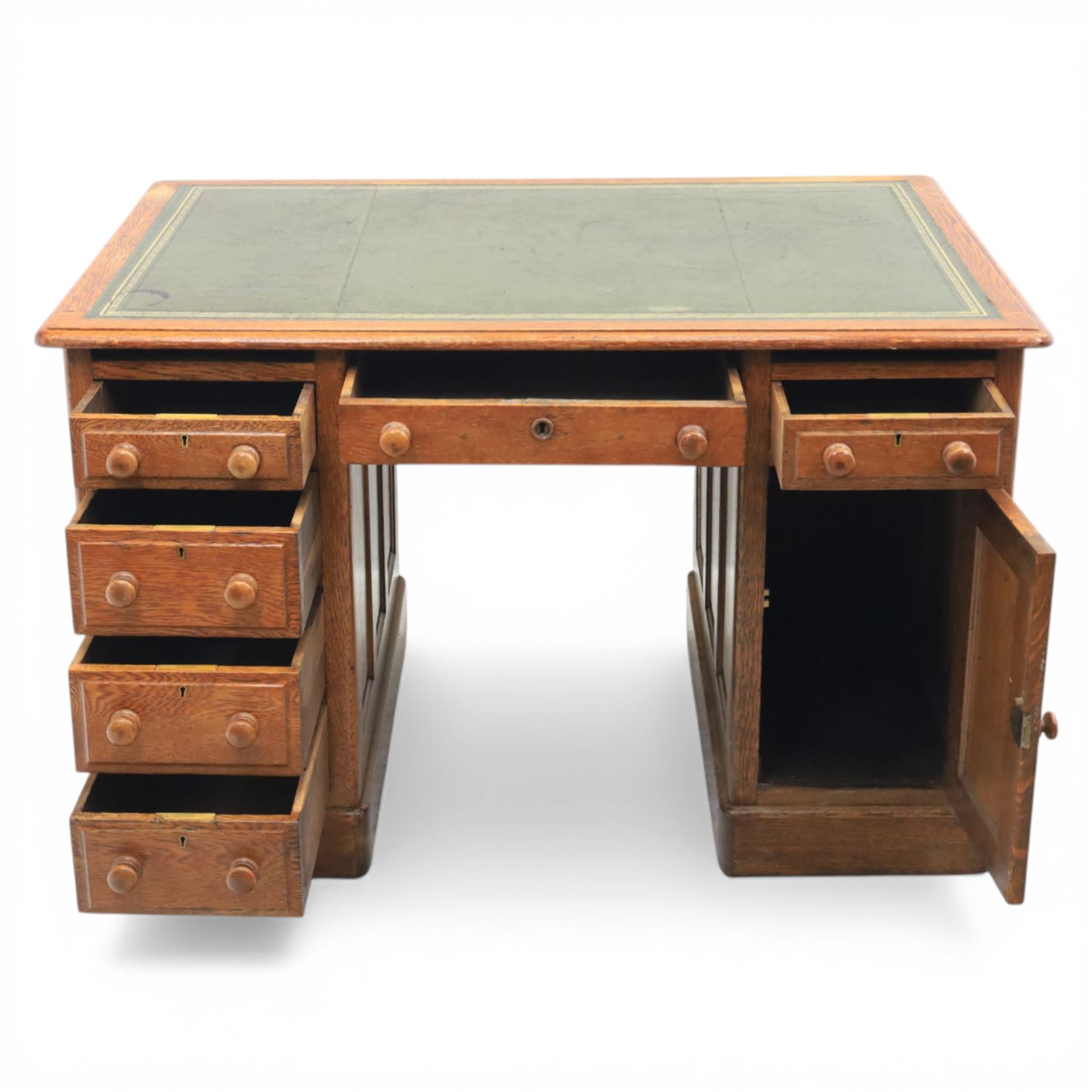 20th century oak compact pedestal desk, tooled green leather inset top, above a single frieze drawer, with a bank of four graduated drawers and a drawer and cupboard, panelled sides raised on castors