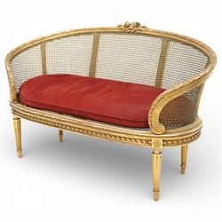 19th century giltwood and gesso settee, with shaped crest rail centred by carved floral detail, the cane back with vertical divisions, upholstered seat with loose cushion, raised on fluted tapering legs