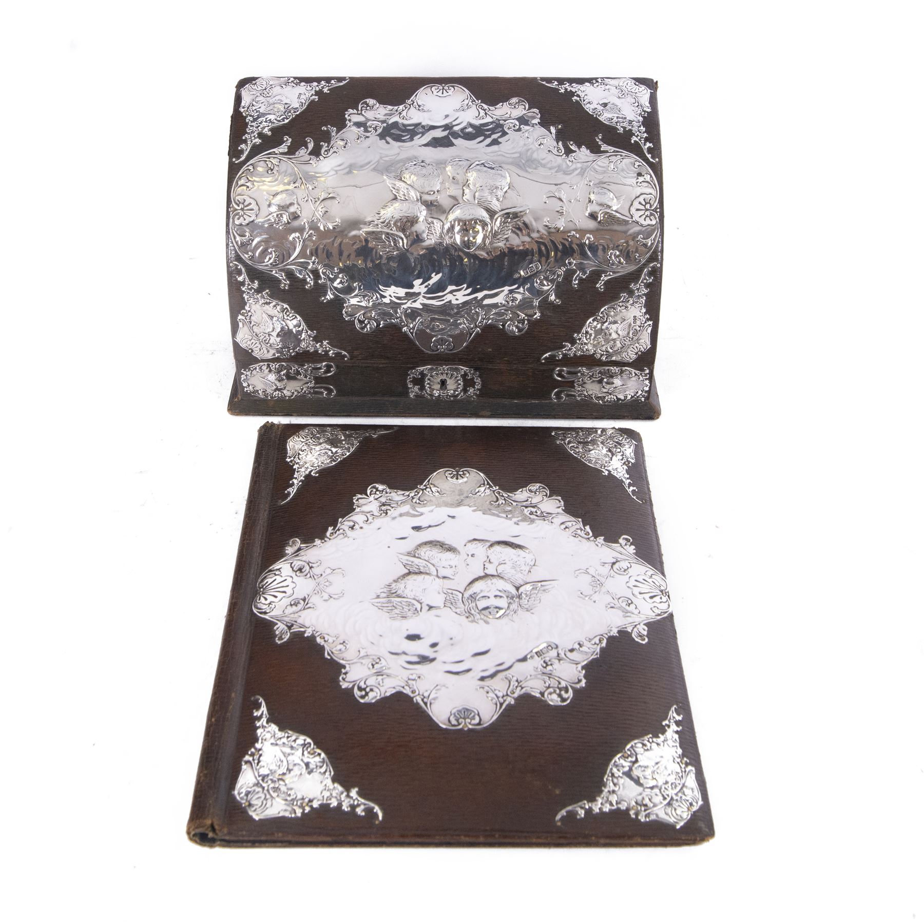 Edwardian silver mounted stationery box and silver mounted blotter, the box of rectangular form with curved front with applied repousse silver panels of putti within a scrolling foliate edge, the hinged cover opening to reveal an emerald green silk lined interior, the blotter with conforming silver mounted panels, each hallmarked William Comyns & Sons, London 1901, box H20cm W31cm D14cm, blotter H32cm W26.5cm