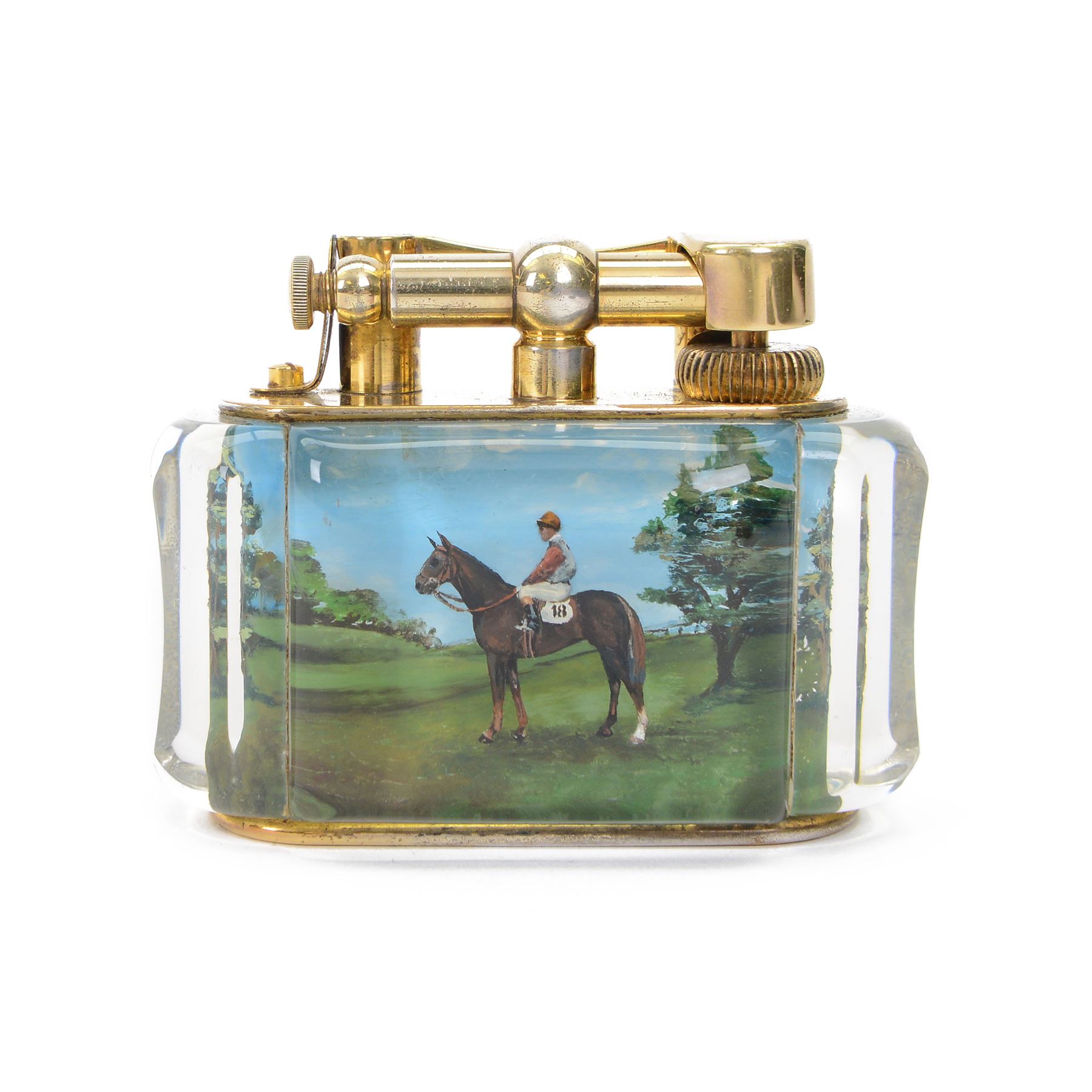 Rare one off special commission Dunhill Sporting Horse Racing half-giant 'Aquarium' table lighter, circa 1955, the lucite panelled body engraved in reverse intaglio technique and hand-painted with Nicholas Nickleby in action, winner of the Royal Hunt Cup, Ascot June 1955, the reverse with jockey Willie Snaith mounted upon Nicholas Nickleby, the gold plated top with arm stamped Dunhill Reg. No 737418, the base stamped DUNHILL LIGHTER, H7.5cm W10cm D5cm

Provenance:
Commissioned by the owner of Nicholas Nickleby, the lighter was gifted to Colin Hetherton, a young veterinary surgeon whose intervention saved Nickleby from certain retirement. Hetherton’s expert care and persistence brought the horse back to full health, culminating in a win that stunned the Ascot crowd.