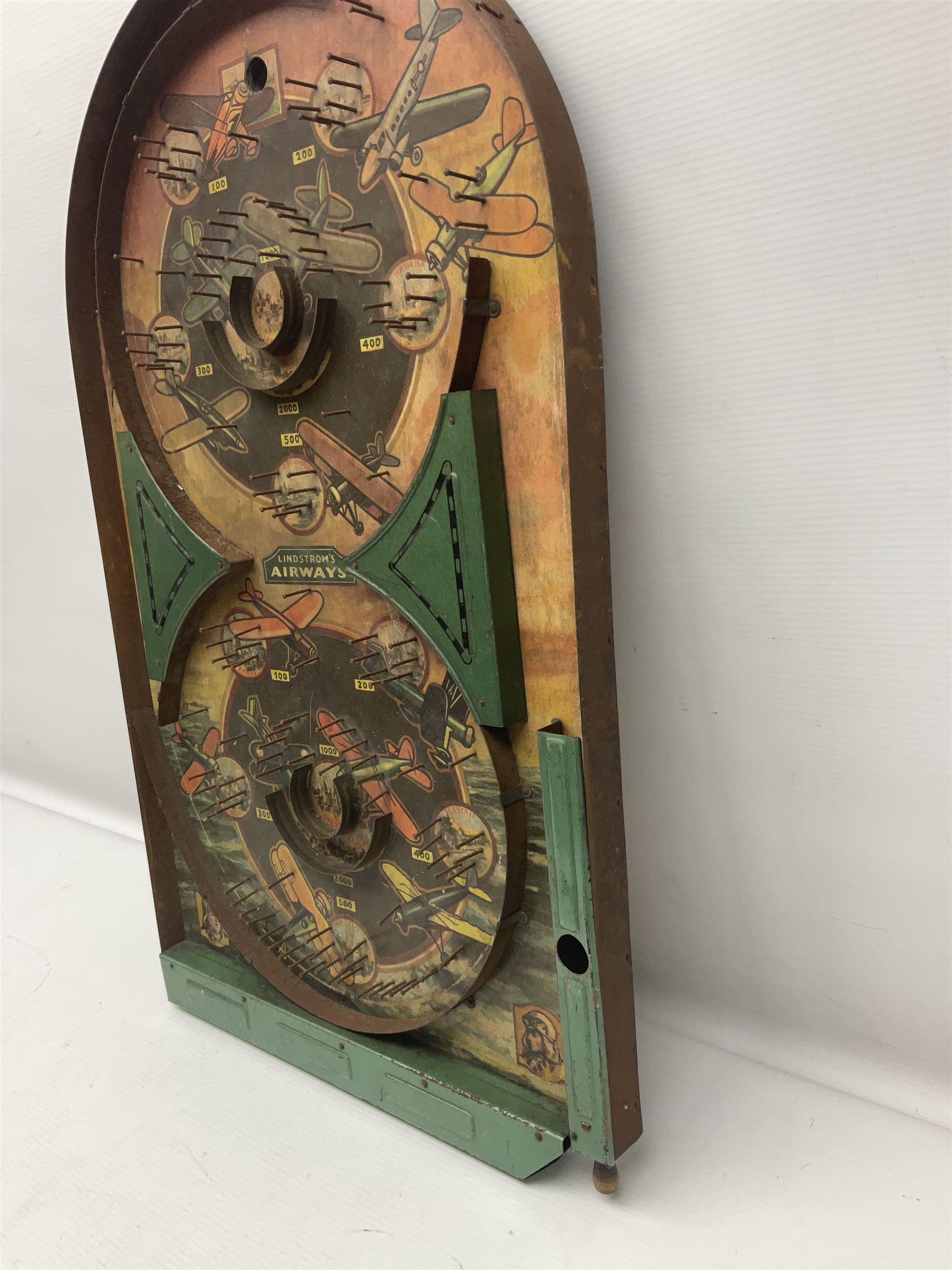1934 Lindstrom's 'Airways' tin-plate bagatelle game by Lindstrom Tool and Toy Company Bridgeport Conn., the decorative bagatelle board depicting Lindstrom's epic airway routes; with wooden peg and quantity of balls H61cm