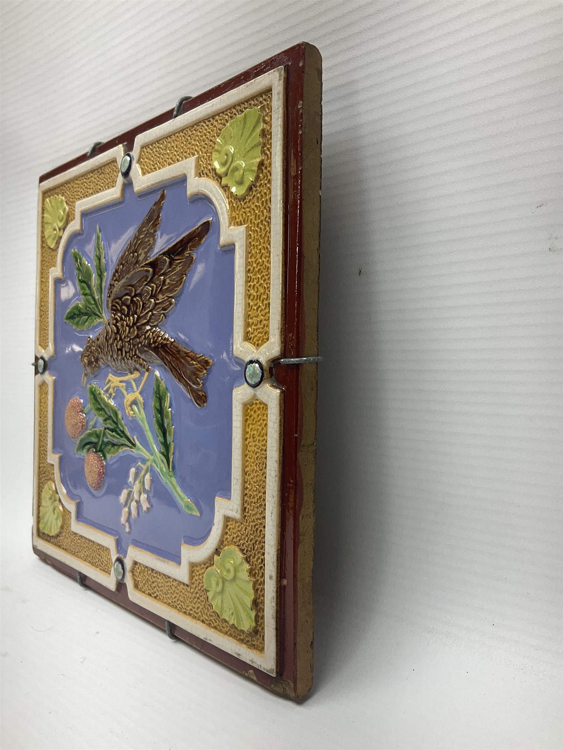 19th century Minton & Co majolica tile, decorated in relief with a bird upon a fruiting branch against a blue ground, with textured ochre border and anthemion to each corner, impressed mark verso, H19.7cm
