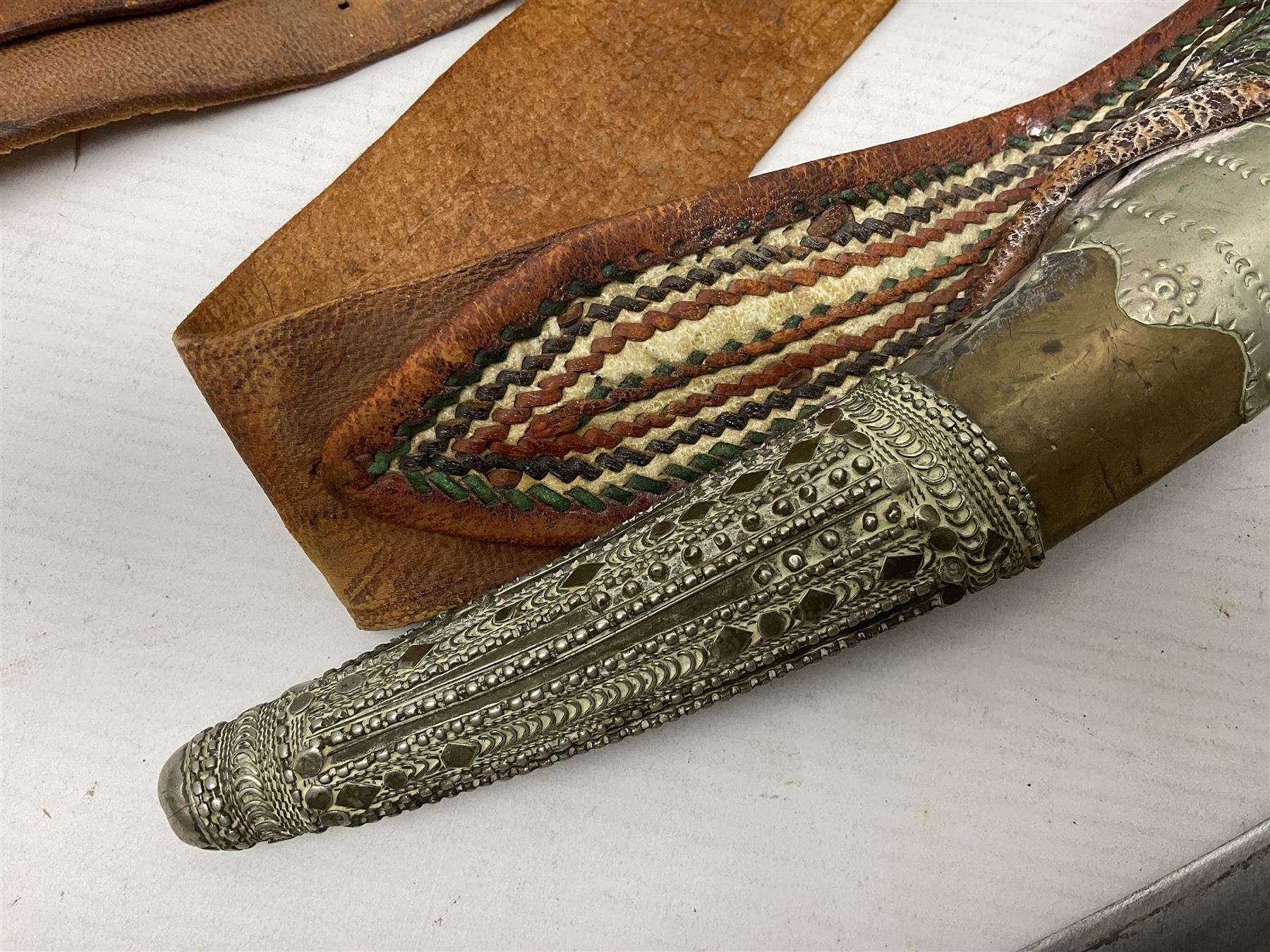 Saudi Arabian khanjar dagger with 29.5cm curving double edged  steel blade; white metal and copper mounted horn grip; in white metal mounted brass and leather scabbard incorporating embroidered leather wearing strap