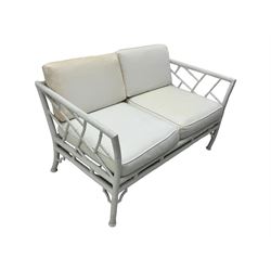 Late 20th century faux bamboo conservatory sofa, white painted frame with geometric openwork back and sides, loose cream cushions, on cylindrical supports (W134cm, D76cm, H80cm); matching armchair (W75cm, D76cm, H80cm); matching coffee table with glass insert (W46cm, D45cm, H36cm)