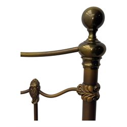 Victorian design king size brass bed frame, featuring an arched headboard and footboard with intricate cast floral and scrollwork centre motifs, flanked by cylindrical supports with ball finials and decorative collars, raised on rounded feet, with a slatted wooden base