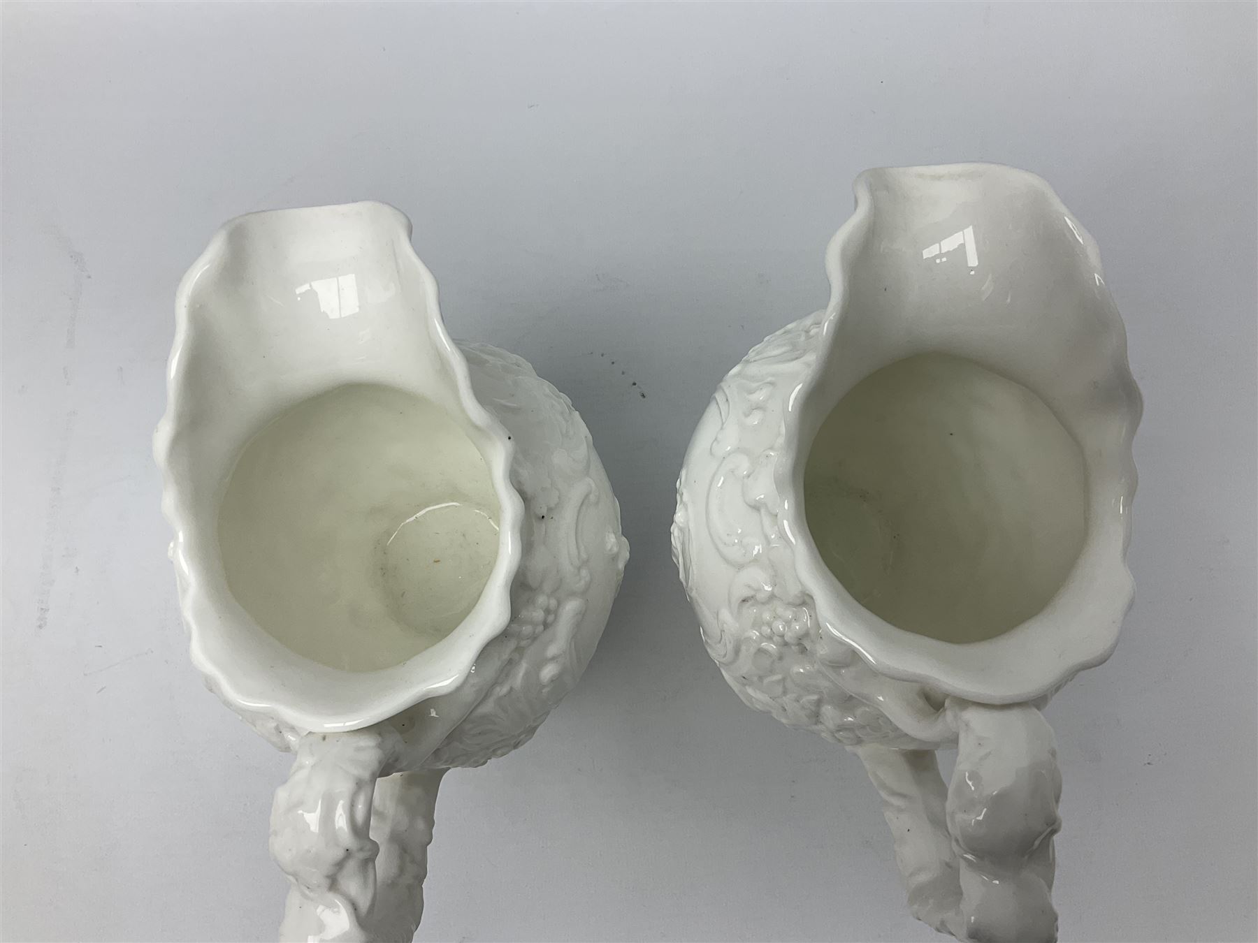 Pair of early/mid 19th century Copeland and Garrett white glazed pitchers, modelled in the Georgian style and moulded with the figures of Venus the Roman Goddess of Love, and Aurora the Roman Goddess of Dawn, within C scroll borders and foliate surround, the naturalistically modelled handle leading to a fruiting vine beneath the rim, upon a spreading base moulded with seashells, with printed green crowned wreath mark beneath, H20cm