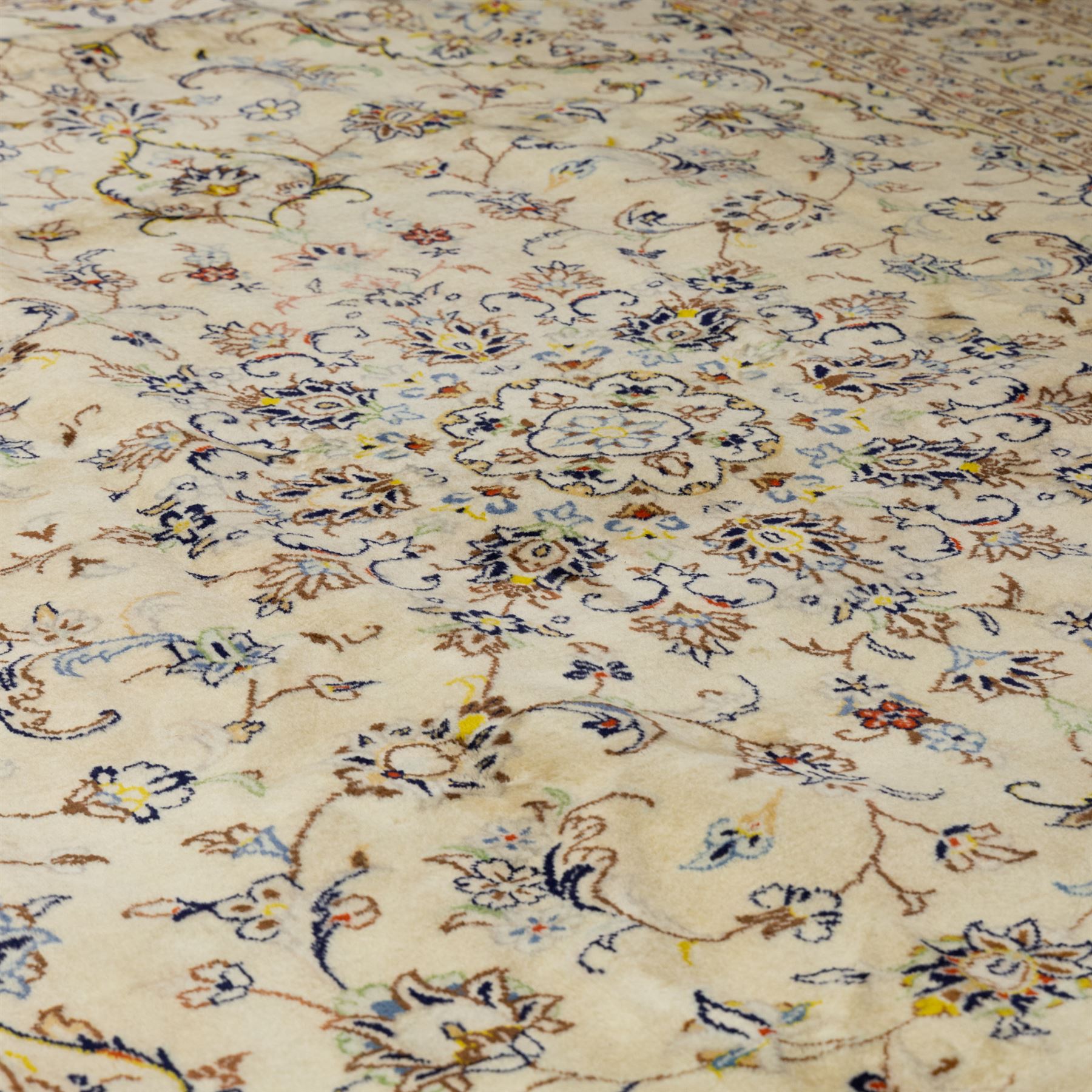 Central Persian Kashan hand-knotted carpet, ivory ground, with a central shaped floral medallion with pendants, surrounded by scrolling foliate and floral motifs incorporating rosettes, palmettes and delicate vine work, enclosed by a conforming ivory border with repeating palmettes and meandering vines, flanked by floral guard stripes, with cotton fringes