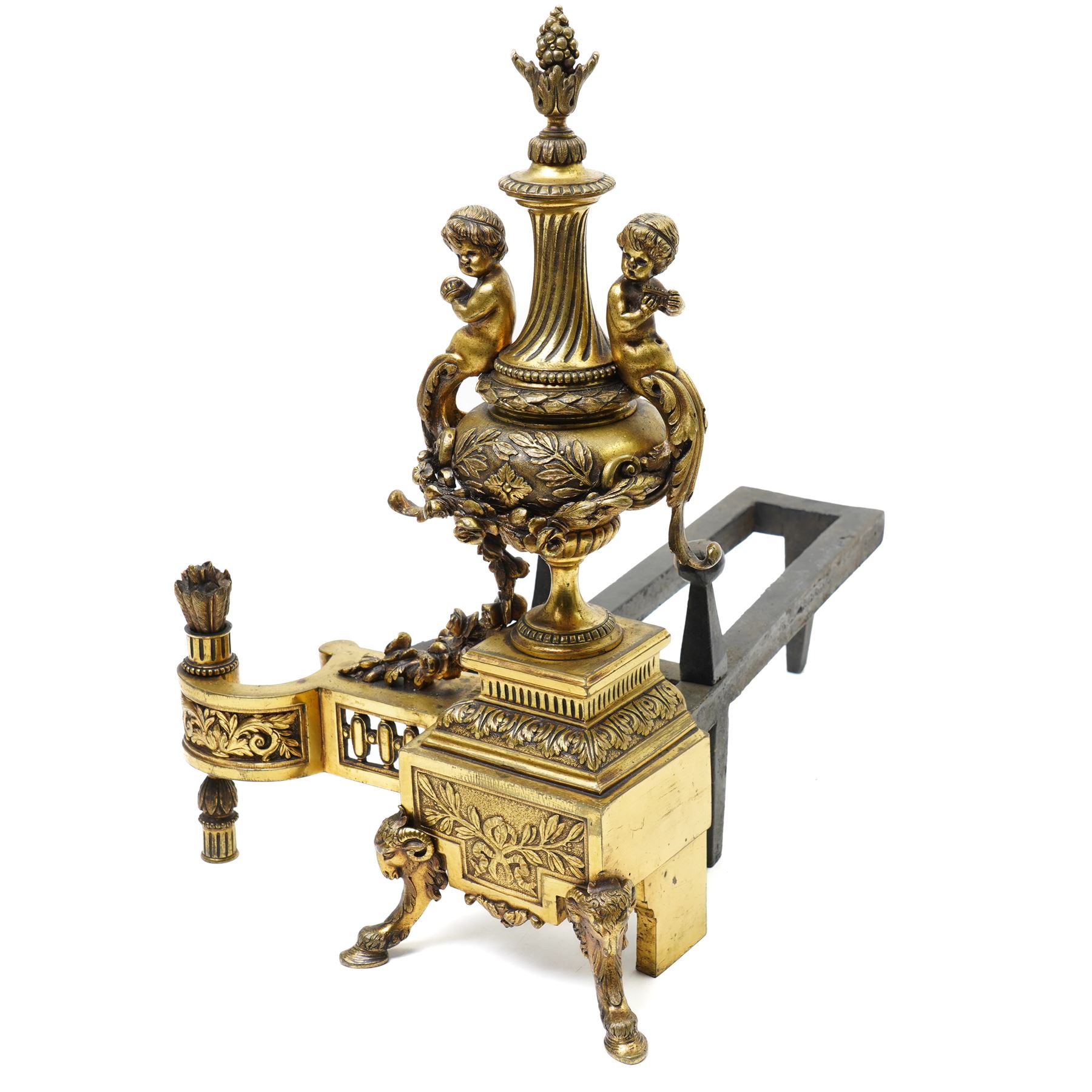 Pair of gilt metal fire dogs, formed as an urn with classical decoration, including putti and floral swags, raised on a square stepped base, the feet formed as rams heads and hoofs, H45cm x W28cm