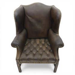 Georgian style leather wing armchair, shaped high back with outscrolled wings above padded arms and deep buttoned seat, close-nailed throughout, raised on square supports united by H-stretcher