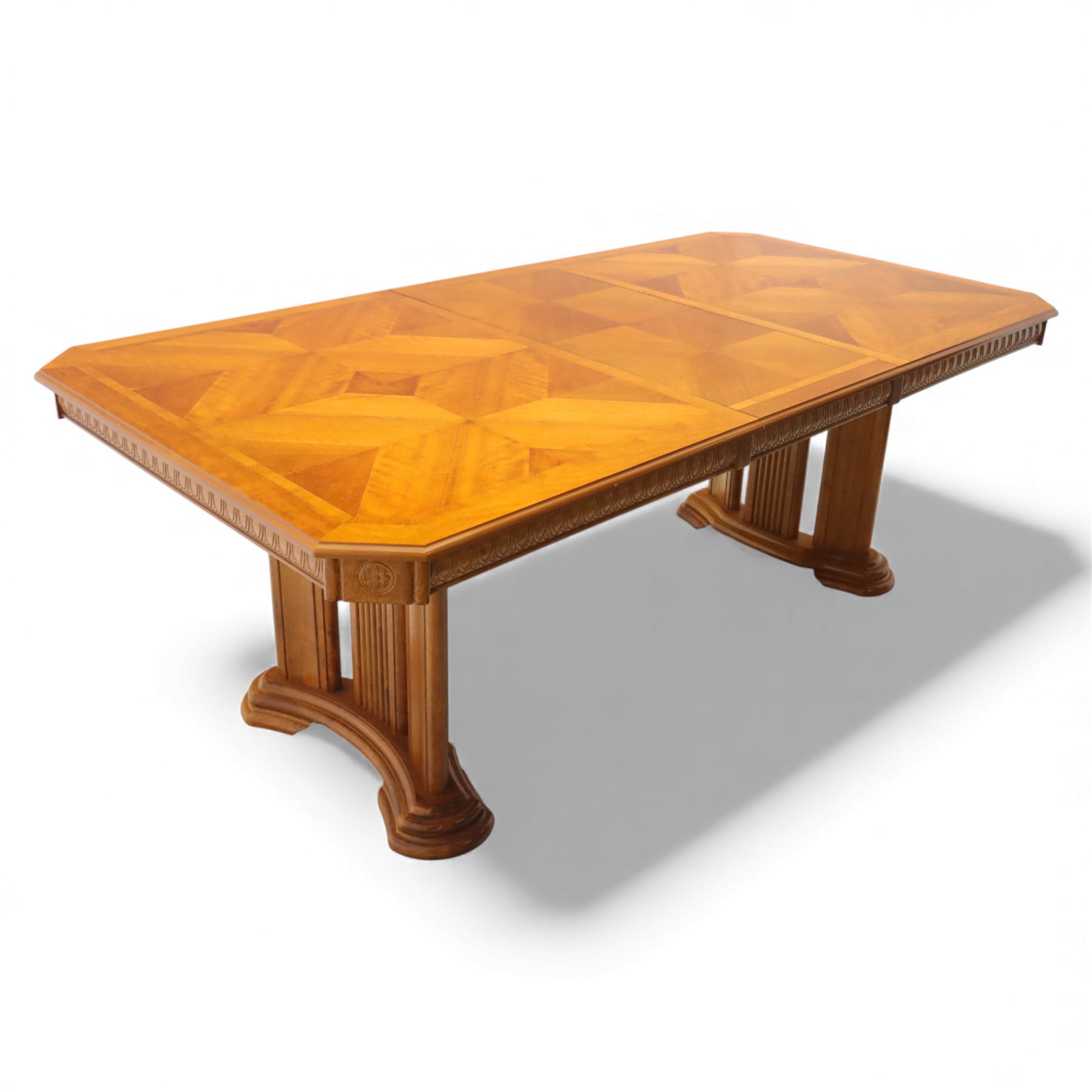 Late 20th century parquetry veneered extending dining table and eight chairs, the rectangular top with canted corners decorated with geometric parquetry panels, moulded edge frieze with repeating carved detail, raised on twin pedestal supports with fluted columns and shaped platform bases, the chairs with pierced splat backs and upholstered drop-in seats
Extends on a central leaf to 208cm