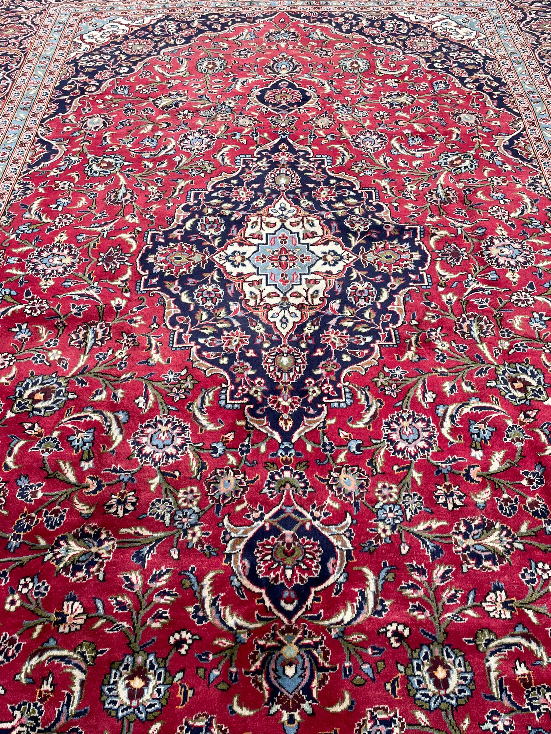 Central Persian Kashan crimson ground carpet, central  floral pole medallion with matching spandrels within a field of scrolling palmette motifs and foliage, the heavily banded indigo border with repeating plant motifs interlaced with scrolled branches