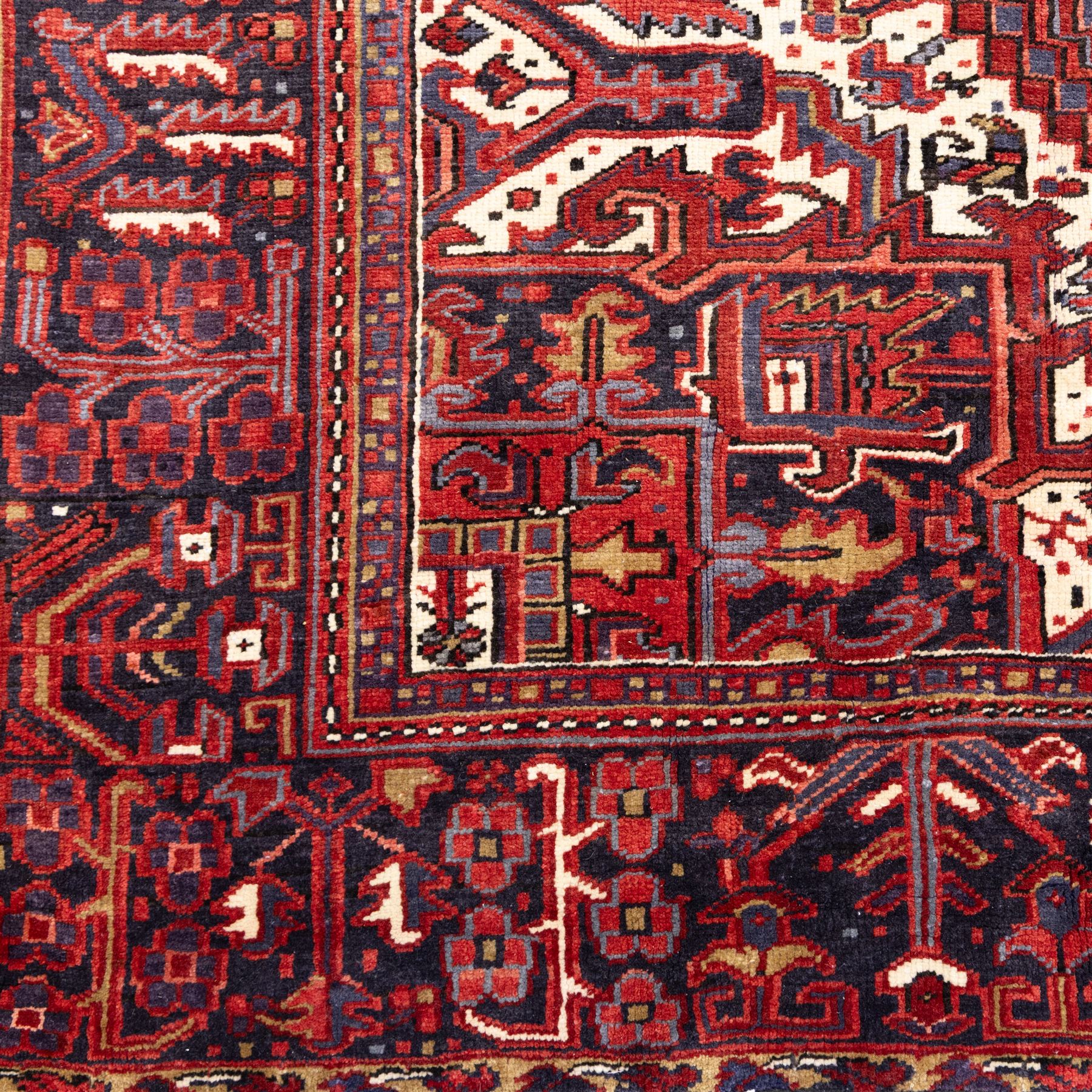 North West Persian Heriz hand-knotted carpet, madder red field with central bold angular steeped medallion with serrated outlines, flanked by stylized palmettes, hooked leaves and geometric motifs, spandrels similarly decorated within a wide geometric border and multiple guard borders in tones of madder red, indigo blue, ivory and olive green, with cotton fringe ends  