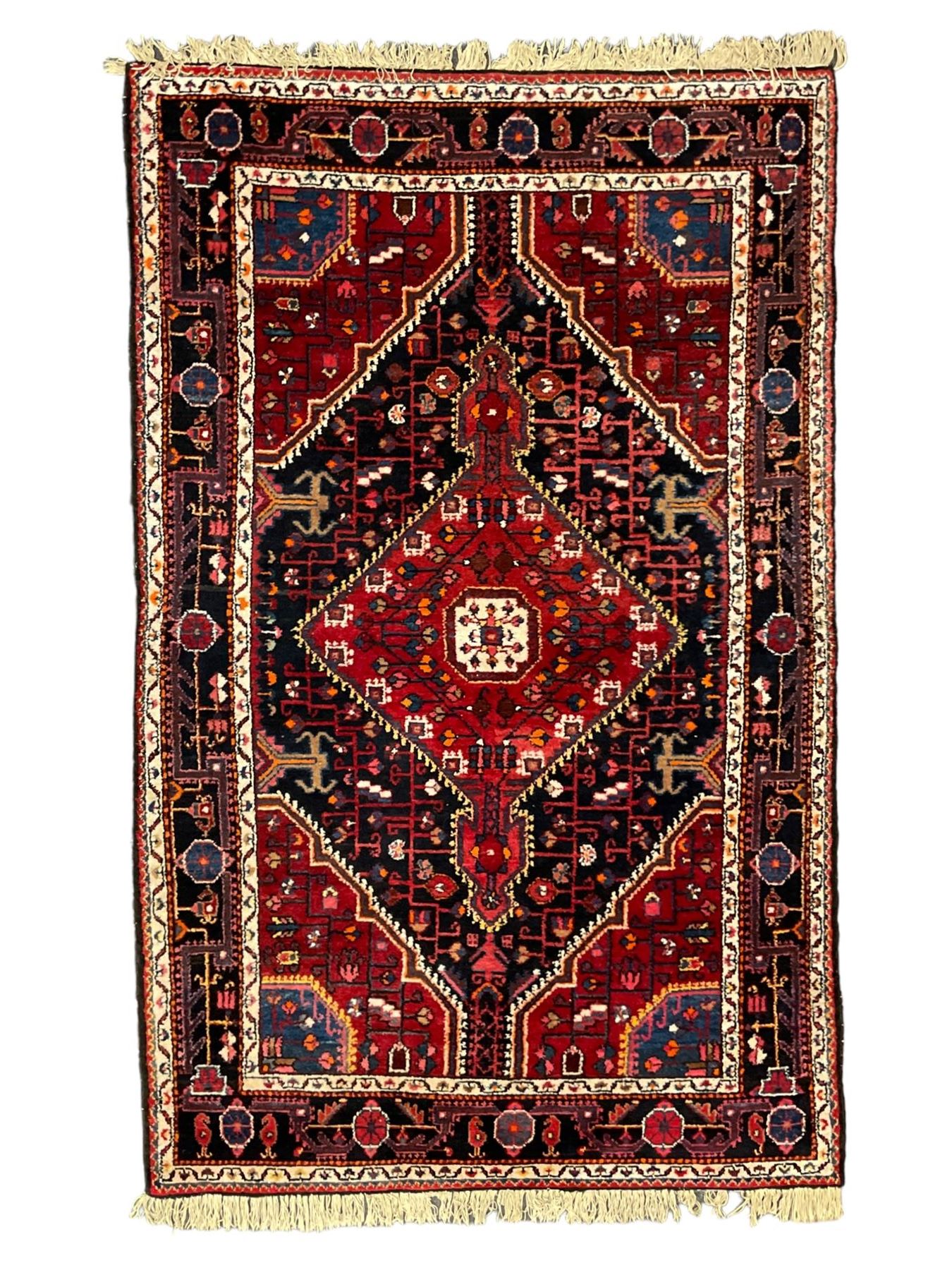 Persian Hamadan red and indigo ground rug, central lozenge medallion with extending poles, the field decorated with interlaced branches and flowerheads, guarded border with stylised floral motifs