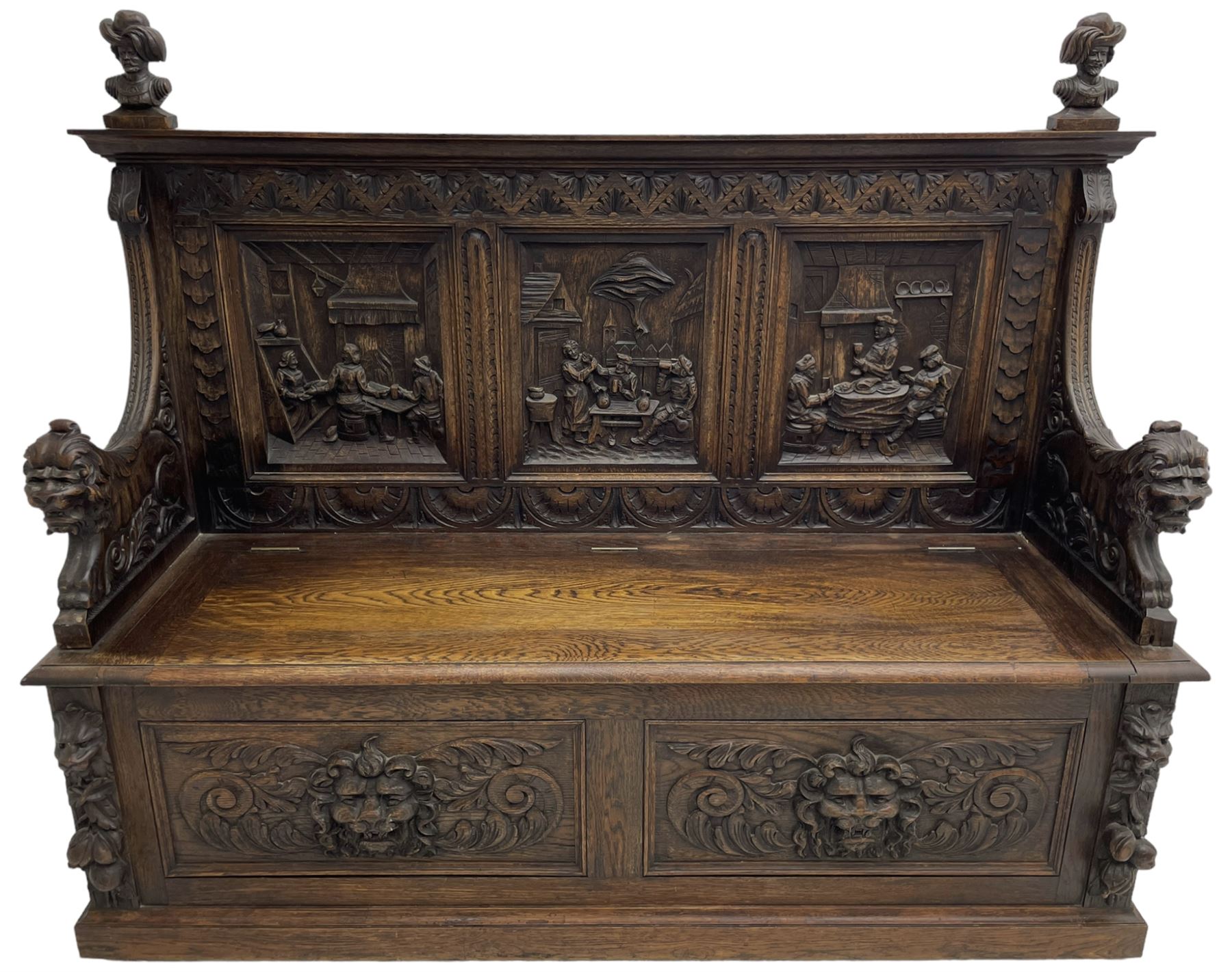 19th century heavily carved oak settle, the moulded upper rail over triangular foliage carved frieze, three Flemish style carved panels depicting tavern scenes, acanthus carved uprights terminating to lion carved arms, hinged box seat, the panelled front carved with lion masks and extending scrolled acanthus leaves, on moulded skirt base