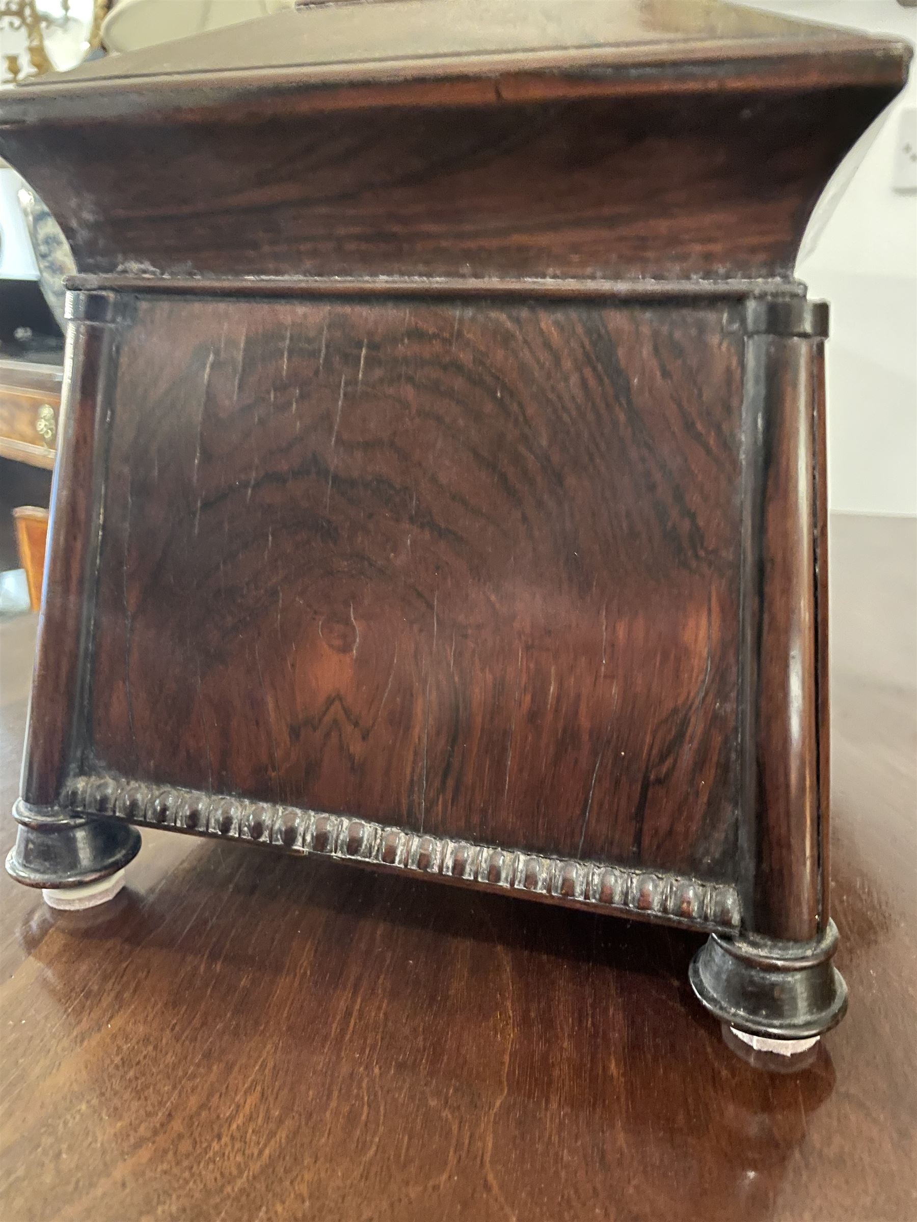 Early 19th century rosewood and brass inlaid tea caddy, of sarcophagus form, the front and hinged opening cover inlaid with brass scrolling panels, opening to reveal a compartmented interior with twin removable boxes with conforming inlaid brass detail to the hinged covers and zinc lining to the interiors, flanking a later glass mixing bowl, the whole upon four turned cylindrical feet, H21cm W36cm D20cm