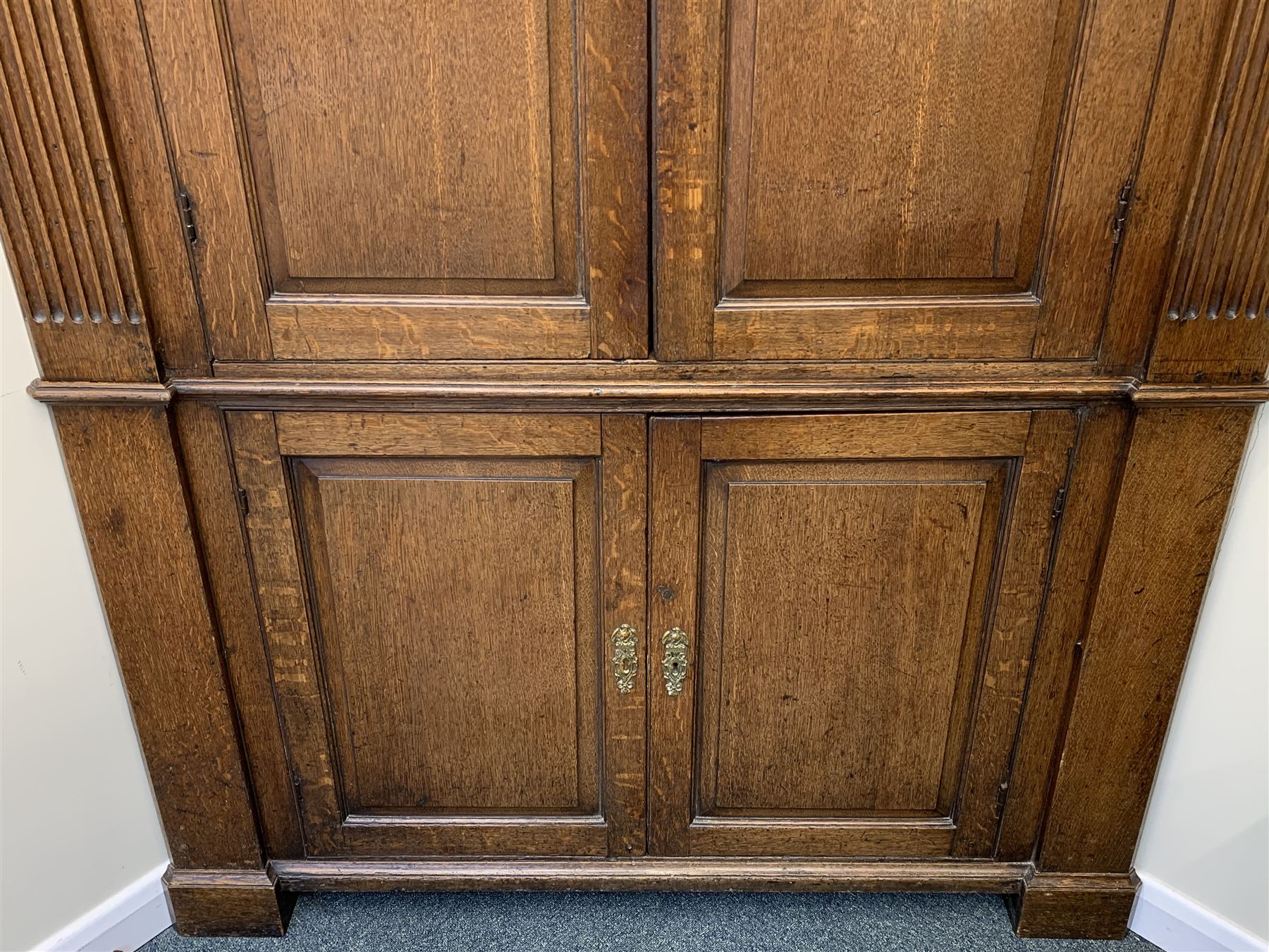 Large George III oak corner cupboard, projecting cornice over two stepped arch doors with fielded panels and blind fret work spandrels, flanked by fluted uprights, cupboard below enclosed by two fielded panel doors, the painted interior fitted with shaped shelves
 