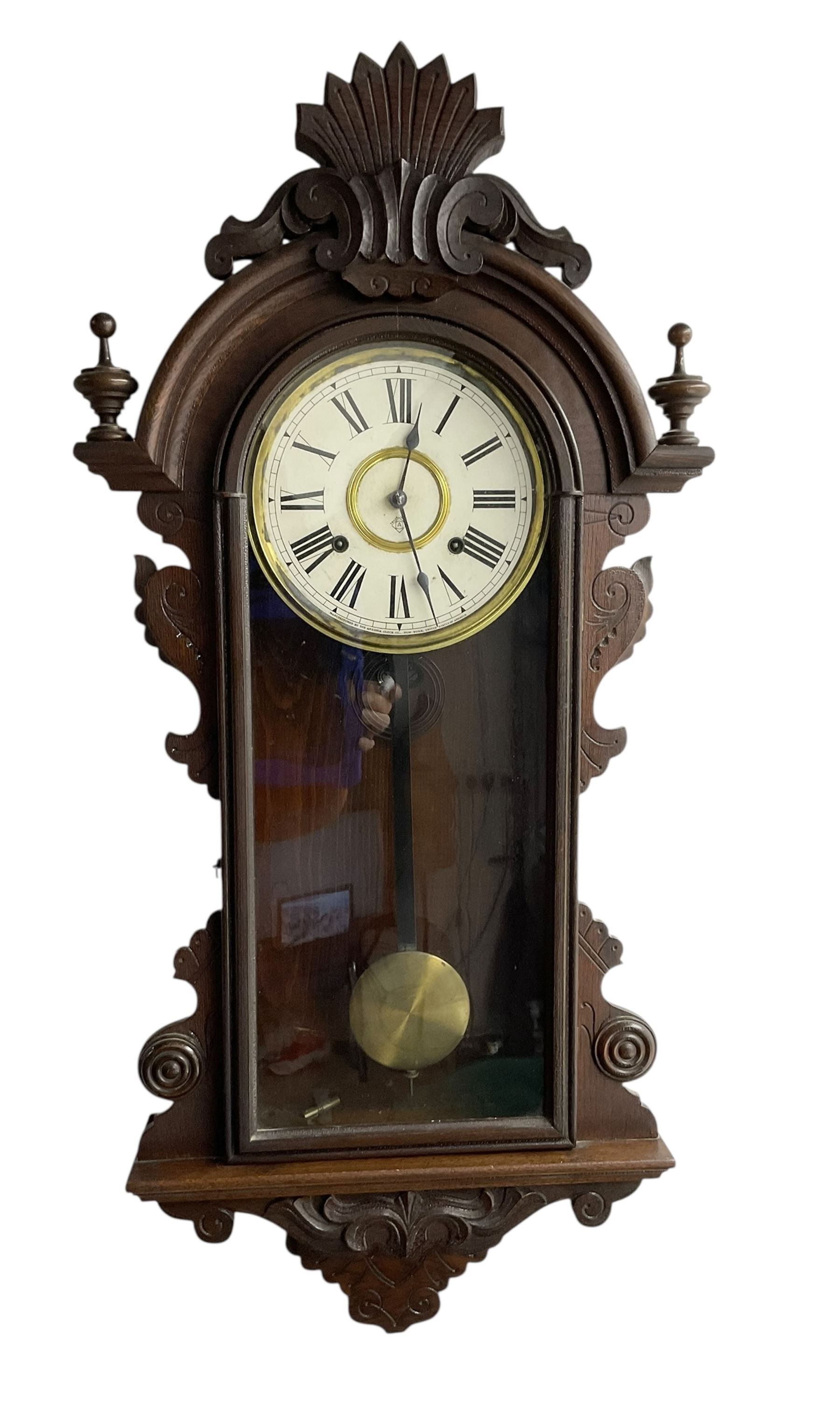 Ansonia-19th century American wall clock in a mahogany case with a carved pediment and base,  turned finials and carved side pieces, with a fully glazed door, dial with Roman numerals and visible pendulum, twin train spring driven movement striking the hours on a coiled gong. With key. 