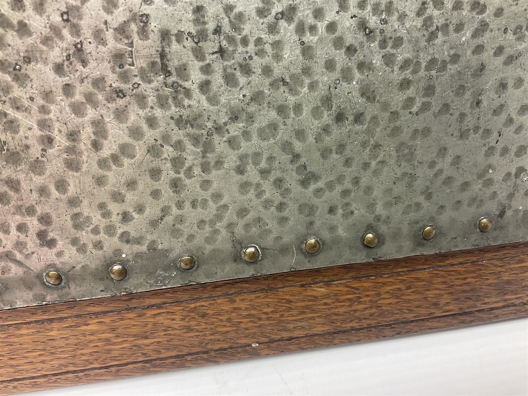 Arts and Crafts oak stand by Arthur Simpson of Kendal, of rectangular form with central hammered pewter panel, surrounded by a border with carved foliate corners, upon two bar supports, bearing label detailed 