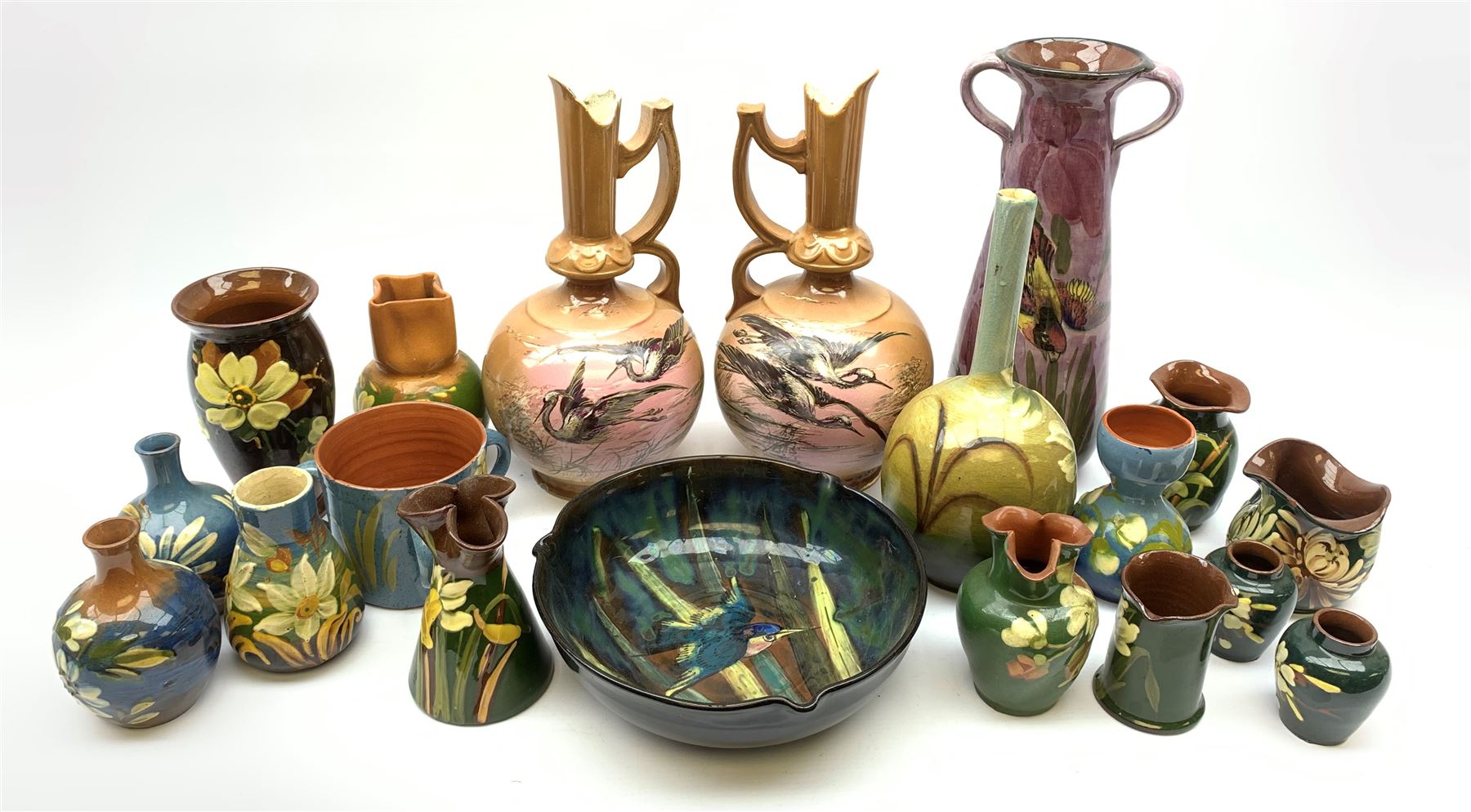 Collection of Devon pottery all having floral slip decoration and include Aller Vale, Watcombe, possibly some Longpark, and other unmarked pieces, tallest H25cm together with a pair of T. Forester jugs hand-painted with cranes and two further Devon pottery pieces, both hand-plated with birds 
