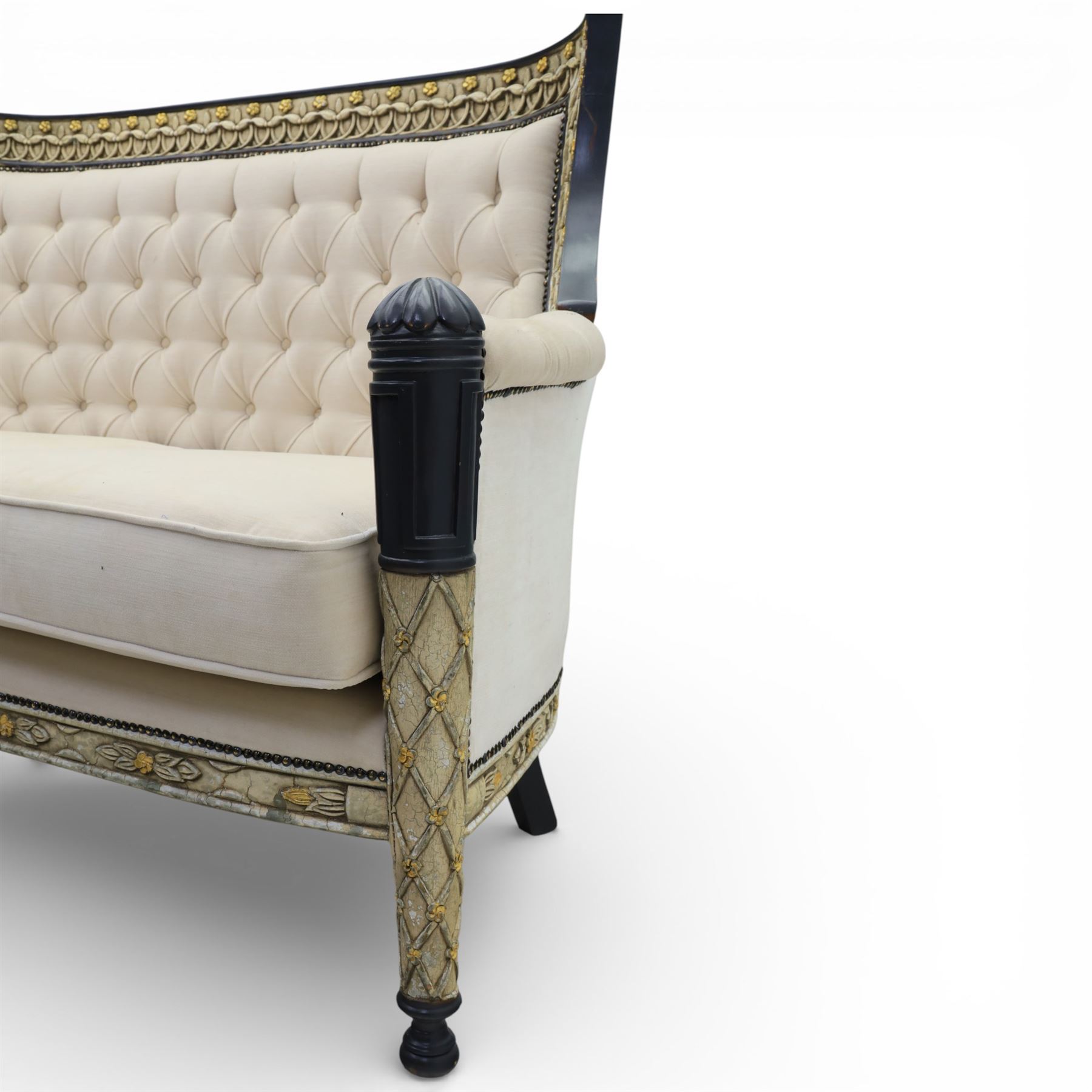 20th century Louis XVI style settee, upholstered in cream fabric with buttoned back and arms, and plain seat cushions, the shaped and black painted frame with entwined foliate detail and gilt flower heads, upon column legs with bun feet