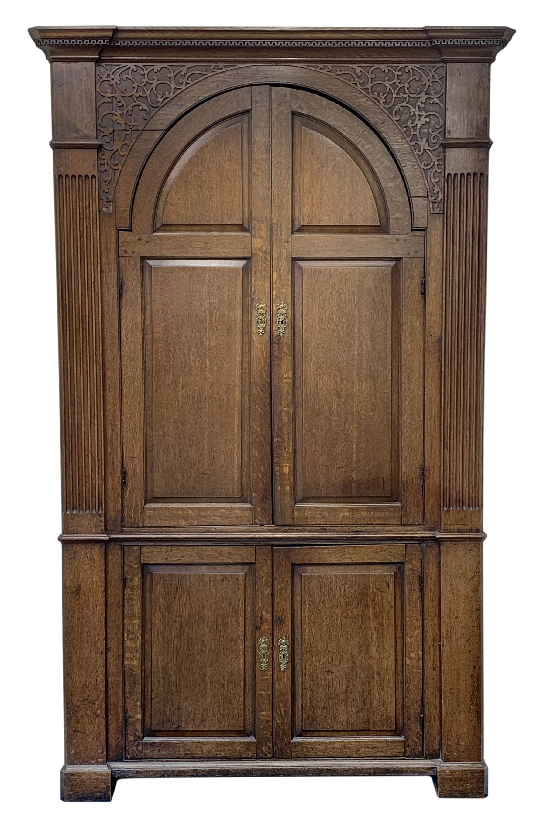 Large George III oak corner cupboard, projecting cornice over two stepped arch doors with fielded panels and blind fret work spandrels, flanked by fluted uprights, cupboard below enclosed by two fielded panel doors, the painted interior fitted with shaped shelves
 