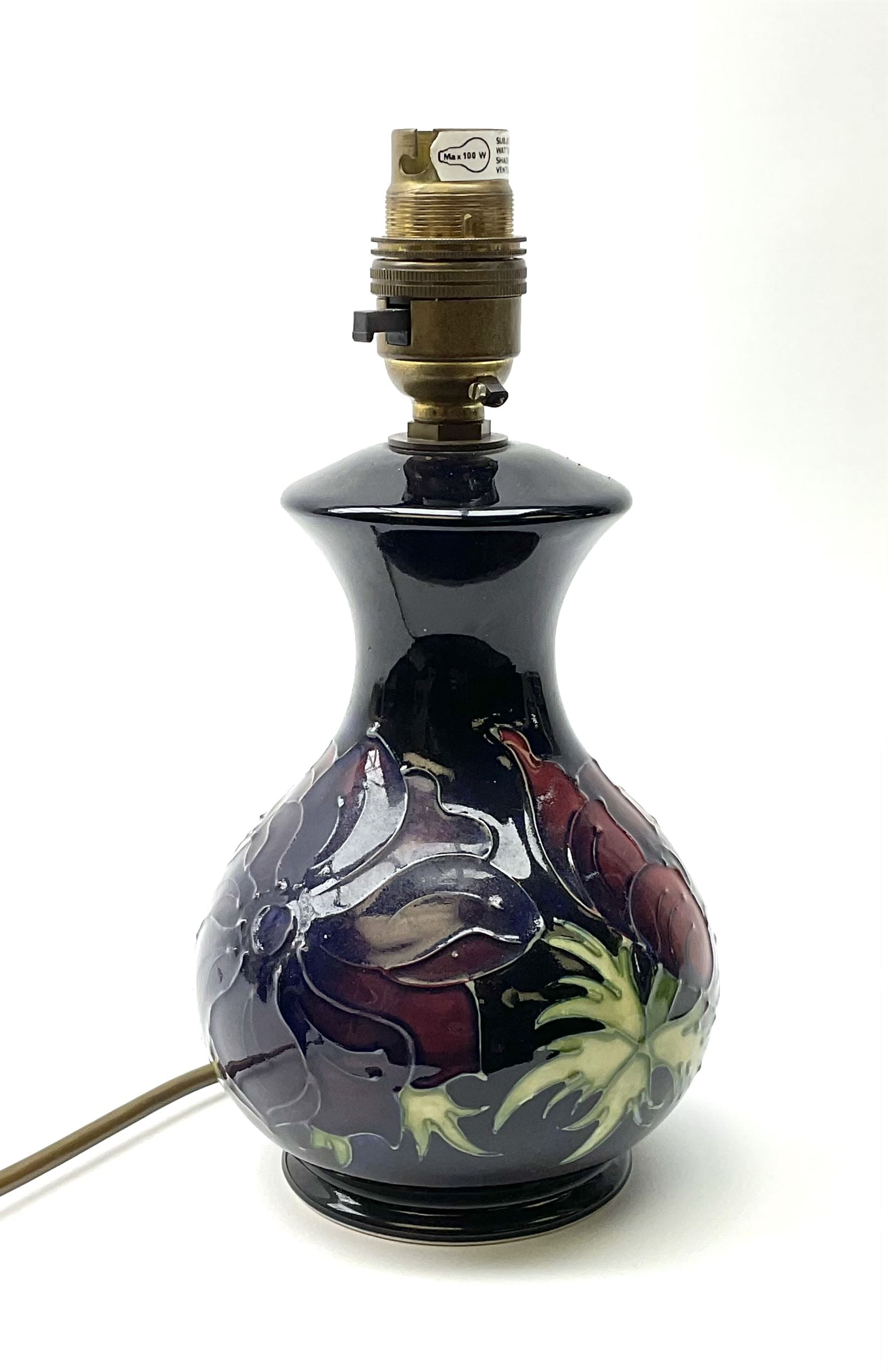 A Moorcroft table lamp, of baluster form, decorated in the Anemone pattern upon a dark blue ground, with impressed marks beneath, with accompanying cream shade with piped detail, overall H38.5cm.