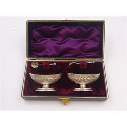 Pair of Victorian silver open salts, of part fluted navette form, with engraved foliate decoration, upon oval stepped foot, hallmarked W H Lyde, Birmingham 1896, H3.5cm, together with a pair of silver salt spoons, with leaf shaped bowls and ball finials, hallmarked Joseph Gloster, Birmingham 1897, together with a pair of Victorian silver open salts, of circular form, with shaped rim and embossed scroll and lattice decoration to the gilded bowl, together with pair of matching silver salt spoons, hallmarked Albert Sydenham, Birmingham 1899, both sets within tooled leather, velvet and silk lined fitted cases