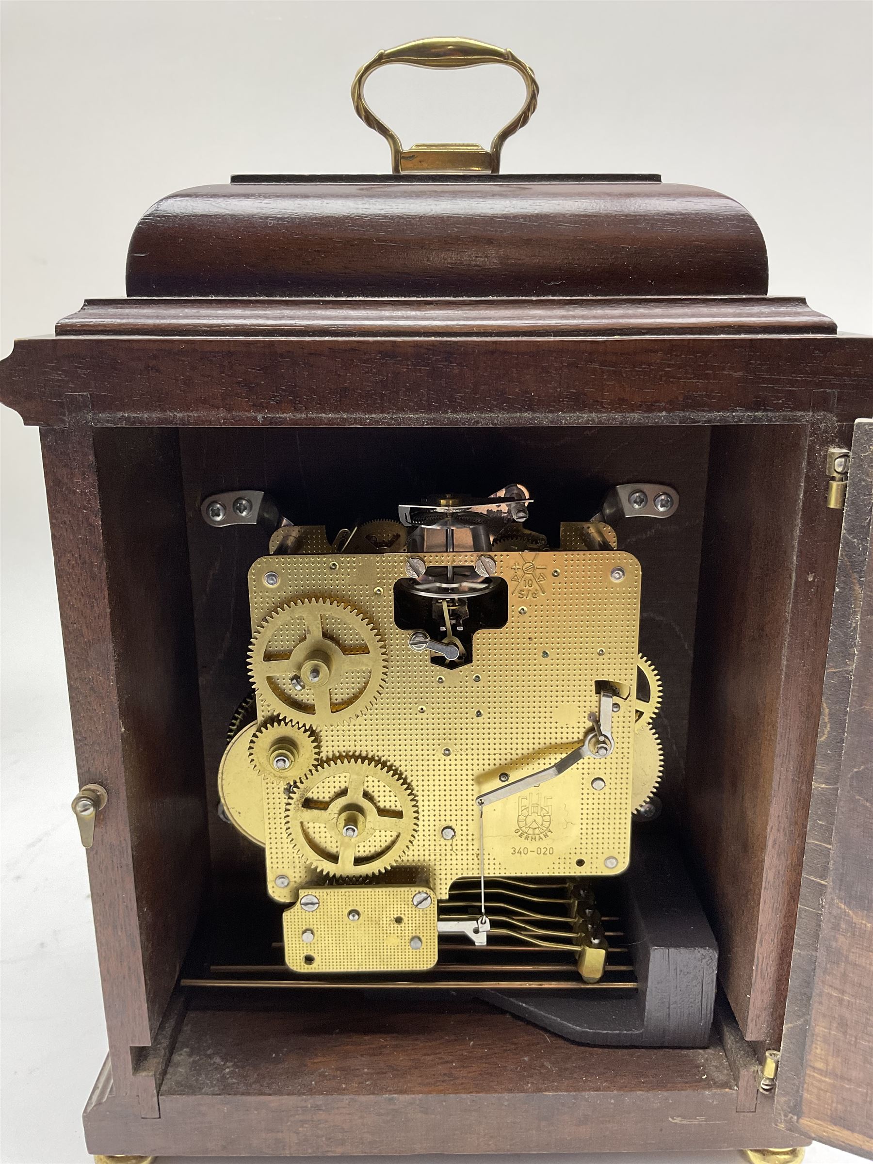 Franz Hermle- 8-day 20th century chiming mantle clock in a mahogany 18th century style case, 
with a bell top and carrying handle, raised on bun feet, brass dial with spandrels and a silvered chapter ring, three train movement striking the quarters on five gong rods, with a floating balance escapement and strike silent feature. With key. 
