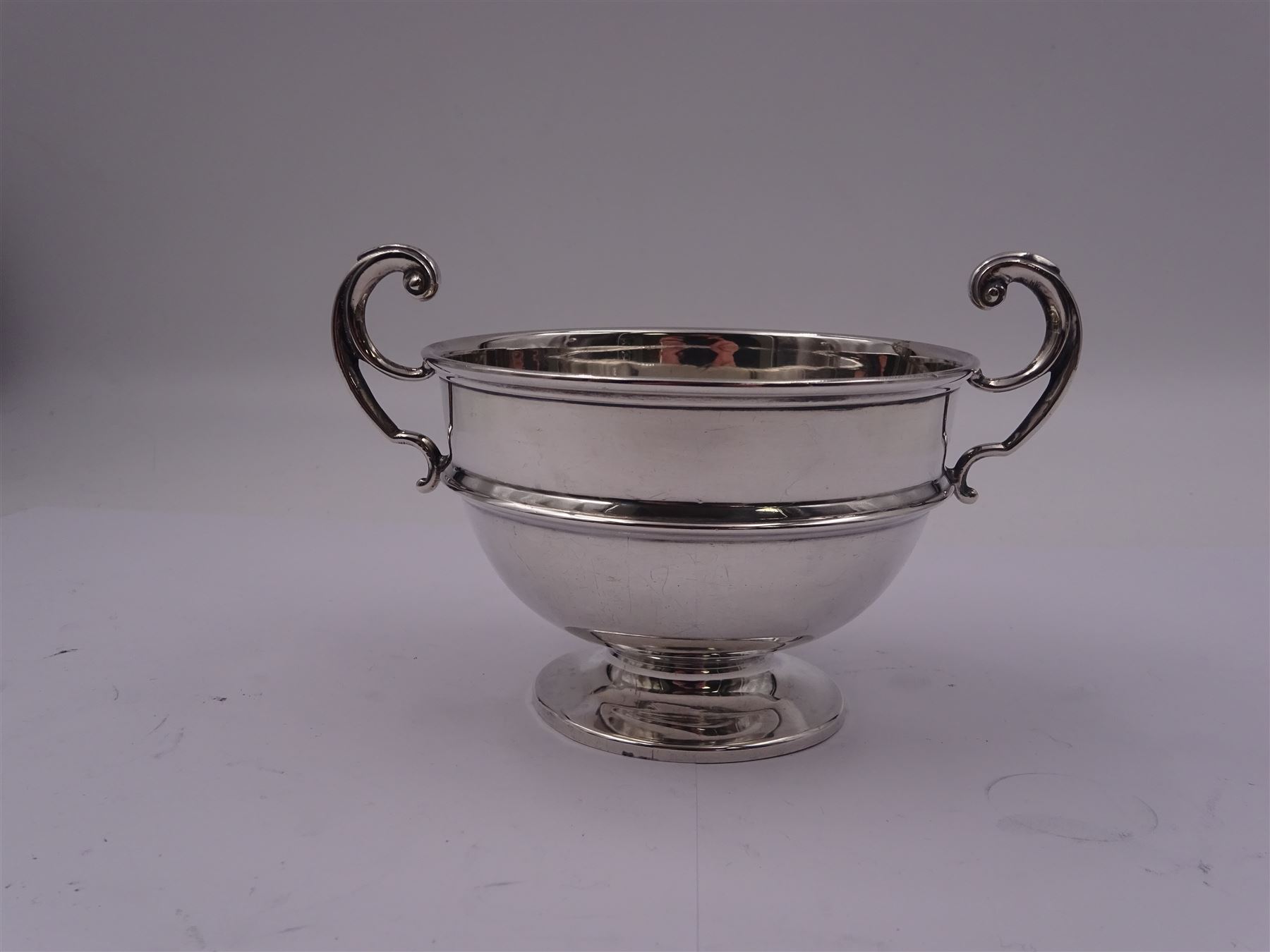 1920's silver twin handled bowl, of circular form with girdle and twin flying scroll handles, upon a spreading circular foot, hallmarked James Woods & Sons, Birmingham 1921, including handles H9cm bowl D10.5cm, approximate weight 4.34 ozt (134.9 grams)
