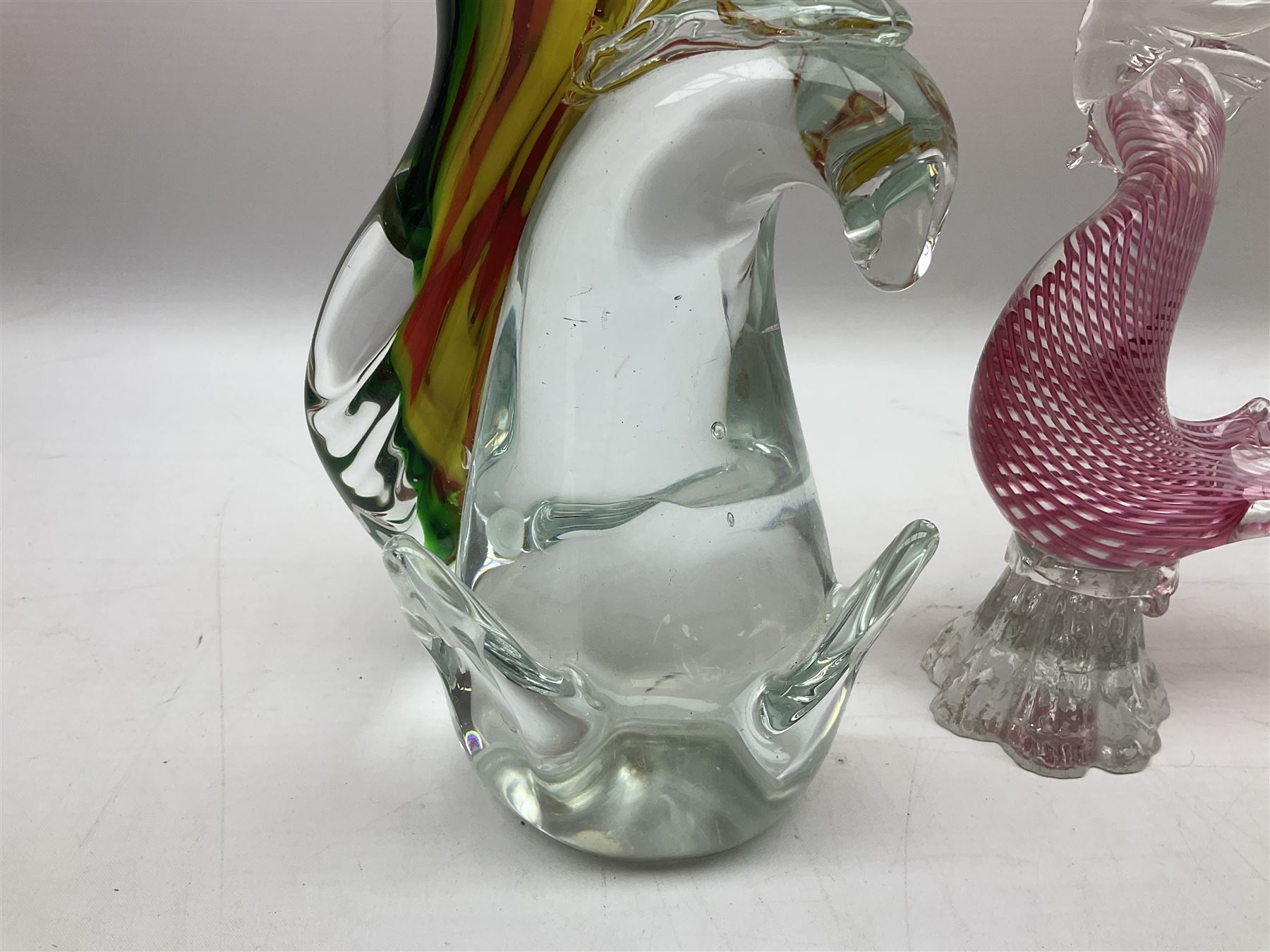 Three Murano style glass cockatoo parrots, the first with mottled yellow, red and orange body, clear outstretched wings, dark blue beak and red crest, raised upon clear stylised base, the second smaller parrot with merging blue and green body, and further with pink striped body, tallest H40cm