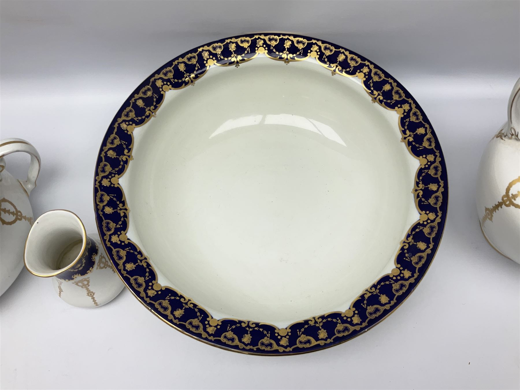 Early 20th century Bishop and Stonier four piece toilet set, comprising washbowl, wash jug, toothbrush pot, and chamber pot, each  decorated with deep blue band and husk swags and festoons in gilt, with printed Caduceus Bisto marks beneath and printed retailers mark 'Manufactured for Harrods Limited London', wash bowl D43cm, wash jug H31.5cm