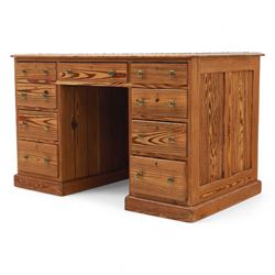 Contemporary stripped and waxed pine pedestal kneehole desk, rectangular top inset with green leather writing surface with brass studded edge, fitted with nine drawers with brass knob handles, above a plinth base on recessed castors