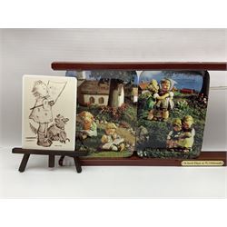 Two ceramic Hummel postcards by Goebel, both displayed on wooden easels, together nine Hummel eggs, set of four Hummel School Days plates, on wooden hanging rack, Goebel Collectors Club Member plaque etc
