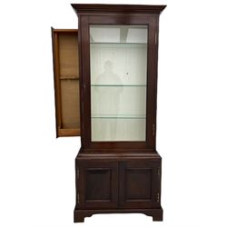 Mahogany display cabinet with hidden compartment, projecting cornice over single glazed door enclosing glass shelves, double panelled cupboard below, the interior with button releasing sliding back compartment, on bracket feet