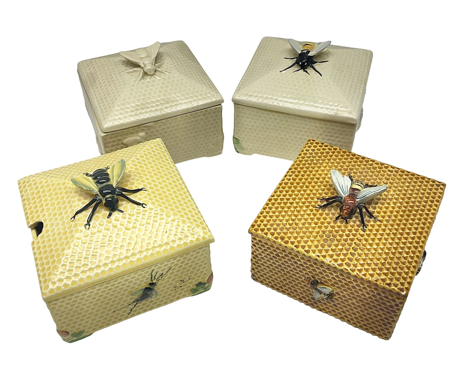 Four square honey boxes with lids,  each decorated with honeycomb pattern and finished with a bee finial
