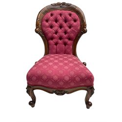 Victorian style mahogany framed nursing chair, the cresting rail carved with fruit and foliage, upholstered in red patterned fabric with buttoned back, on cabriole supports with scrolled terminals