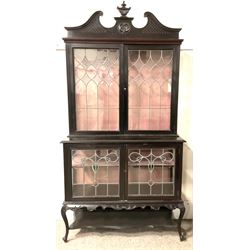 Late 19th century mahogany Empire style display cabinet, swan neck pediment and carved urn finial over two lead glazed doors enclosing two shelves, two glazed doors under, raised on cabriole front supports