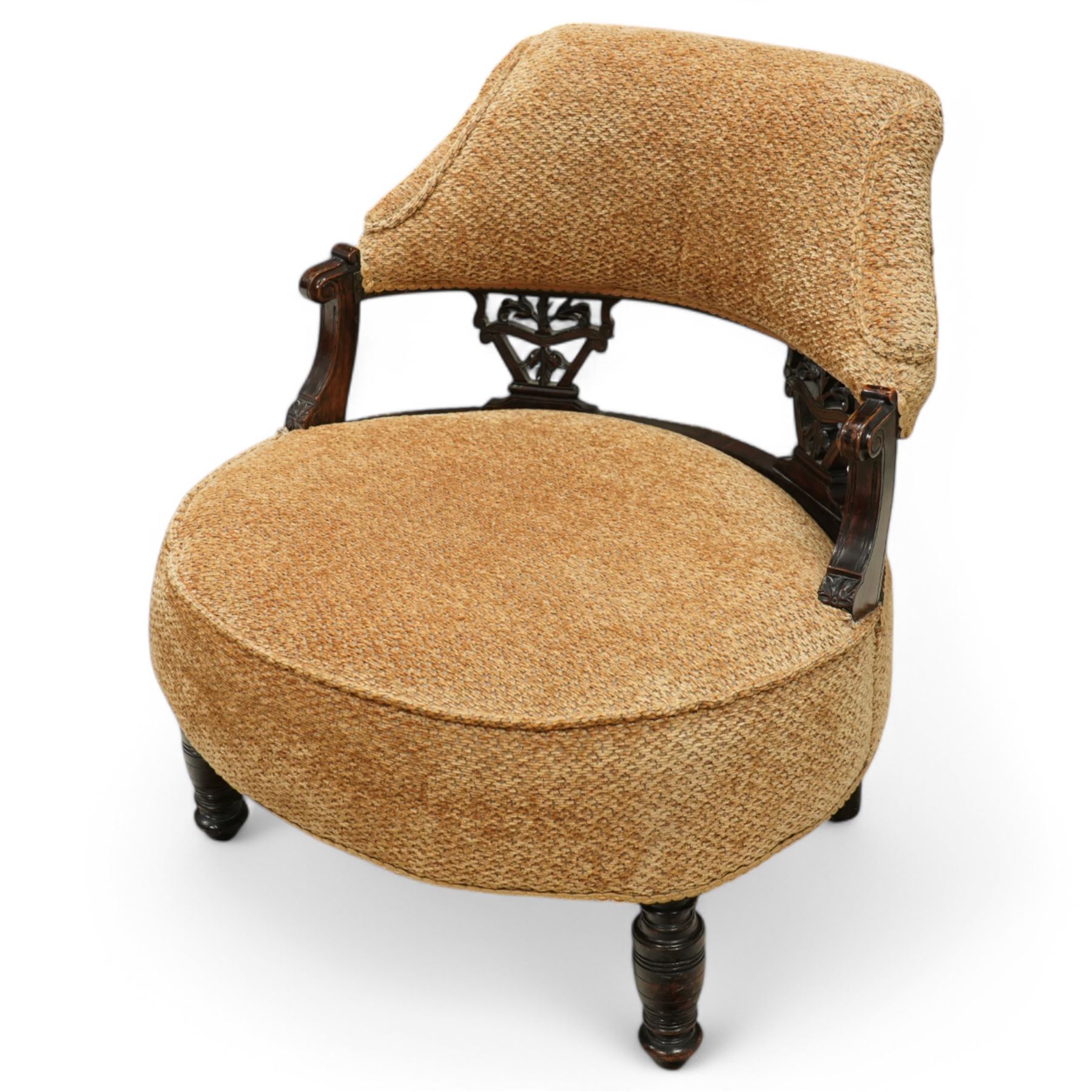 Late Victorian mahogany framed tub shaped chair, curved padded back and overstuffed seat in textured ochre fabric, pierced mahogany back supports with foliate and scroll carving, on turned front legs