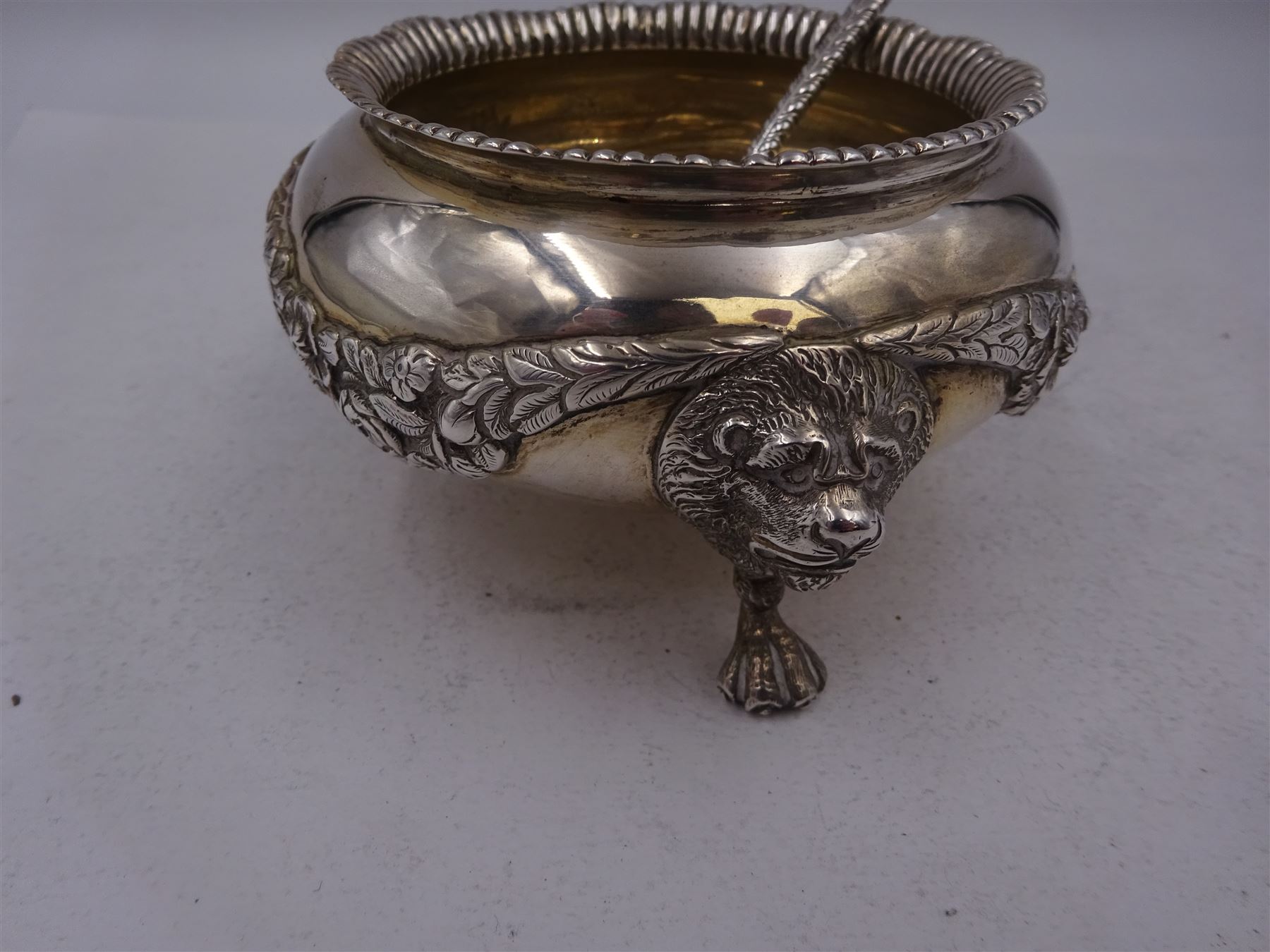 Early 20th century silver open sucrier, of circular form, with fluted gadrooned rim and decorated in relief with floral swags, united by three lion mask mounts and upon three paw feet, hallmarked Z Barraclough & Sons, London 1912, H6cm, D11cm, with similar spoon with lion mask finial, hallmarked London 1912, maker's mark indistinct