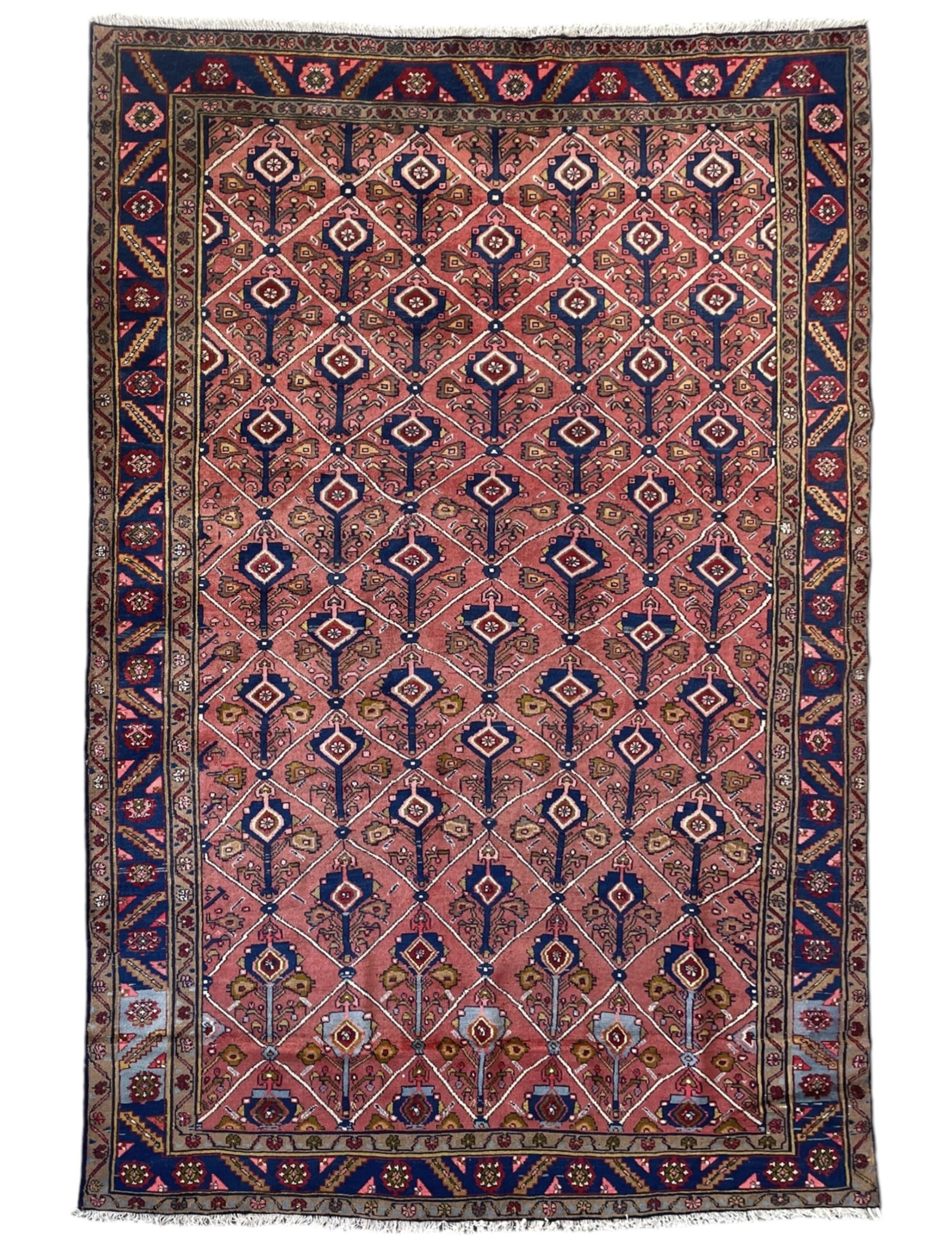 Persian Ardakan crimson ground rug, the field divided by lattice and decorated with stylised tree of life motifs, the border decorated with geometric flower heads, within guard stripes 