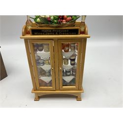 Collection of miniature dolls house grocery shop furniture and produce, comprising glazed corner counter with brass style cash register, shelved preserves unit, pies, cheese board and trays of meats, pair of white cheese counters, biscuit display with six tins, glazed preserves cabinet, pair of shop chairs and four further cheese boards complete with grapes and label flags