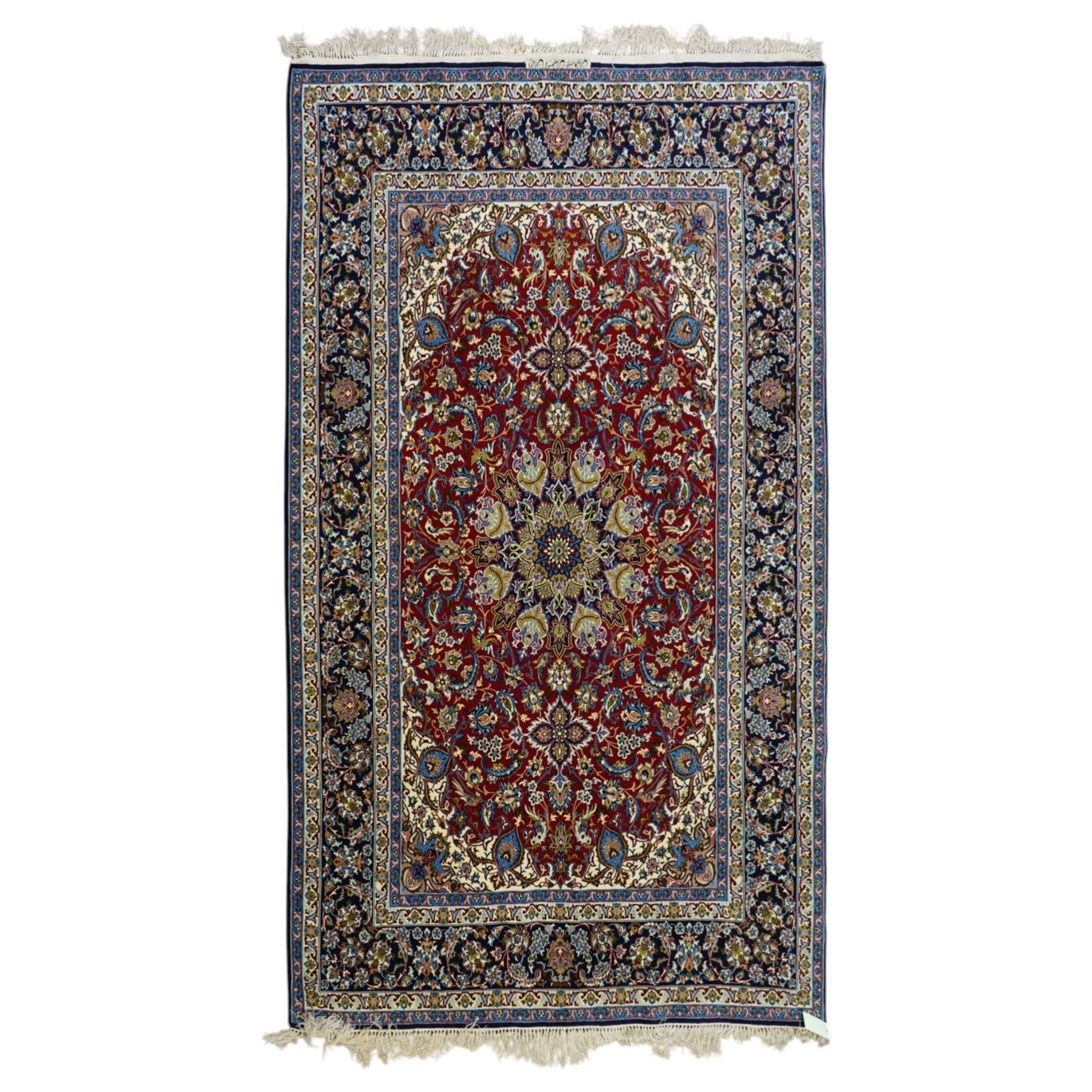 Fine Central Persian Isfahan hand-knotted rug, madder red field with central finely drawn foliate medallion issuing an intricate all-over scrolling vine design with palmettes and arabesques, enclosed by multiple conforming borders in navy ground, signed Isfahan in cartouche, silk fringe ends 