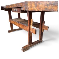 Large early 20th century rustic stained reclaimed pine workbench, the substantial plank top with recessed tool well and two homemade wooden screw vices, above a single frieze drawer and slatted undertier, raised on trestle end supports