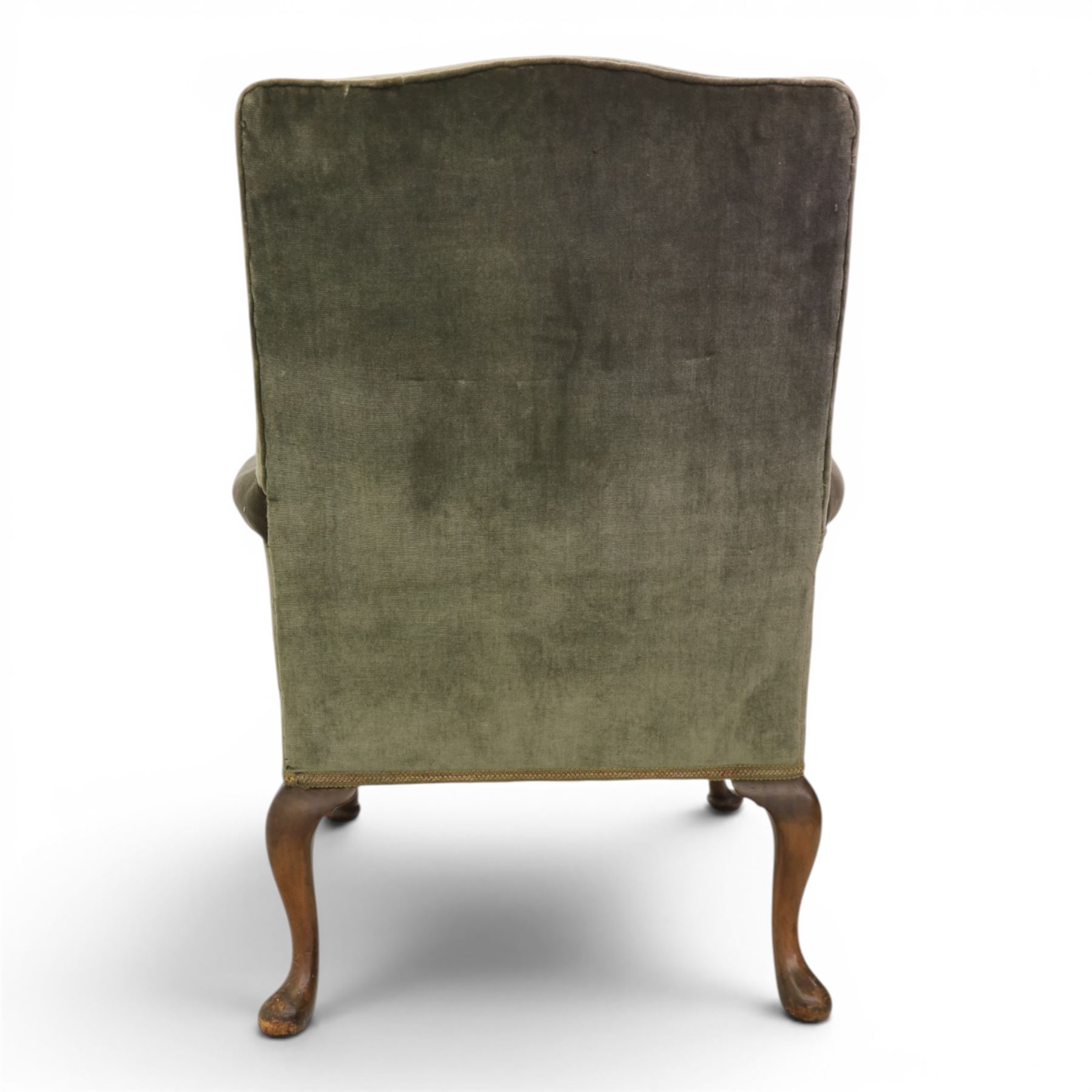 Pair of Georgian style wing armchairs, upholstered in green velvet, each with shaped wing backs, padded scroll arms and loose seat cushions, raised on cabriole supports terminating in pad feet, one with tasselled fringe