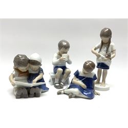 Four Bing & Grondahl figures, comprising an example modelled as a boy and girl reading, no 1567, an example modelled as a girl seated with doll, no 1526, an example modelled as a girl with a dog, no 1779, and a further example as boy seated holding a mug, no 1713, each with painted and printed marks beneath. 