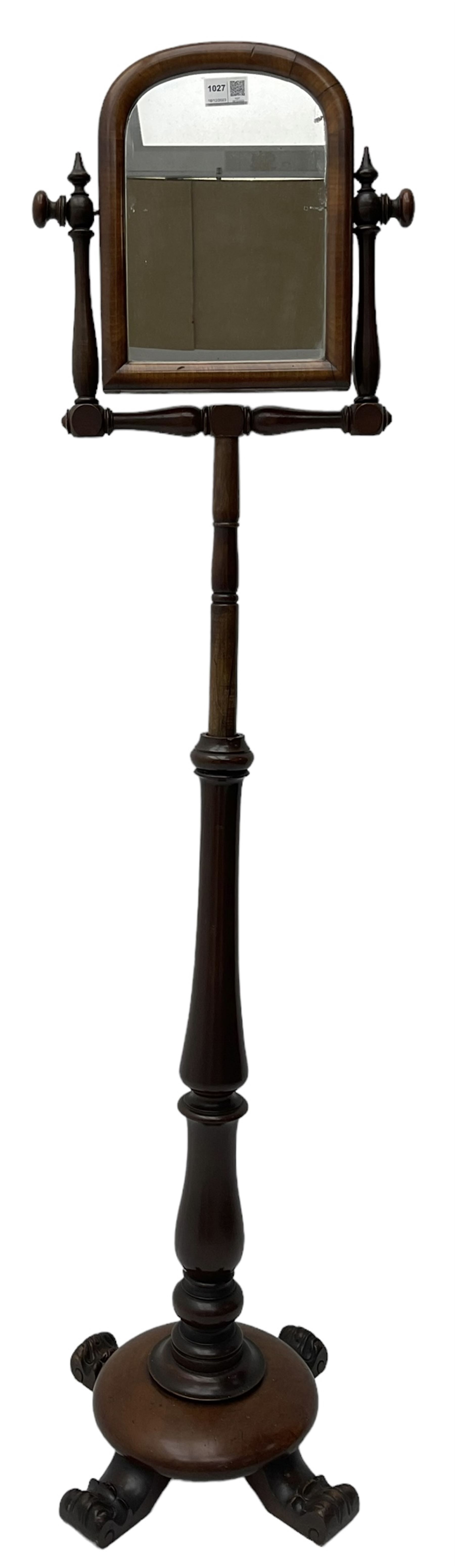 Early Victorian mahogany shaving mirror, arched frame with plain mirror plate on turned horns and supports, adjustable height mechanism on turned stem, circular platform base with four extending block feet carved with scrolled foliage 