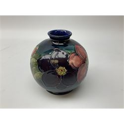 Three pieces of Moorcroft pottery, comprising squat baluster form vase in the Clematis pattern, upon a dark blue and green ground, bowl in the Pansy pattern upon a blue ground and a tapering mug in the Leaf and Berry pattern upon a dark green ground, each with printed marks beneath, tallest example H11cm